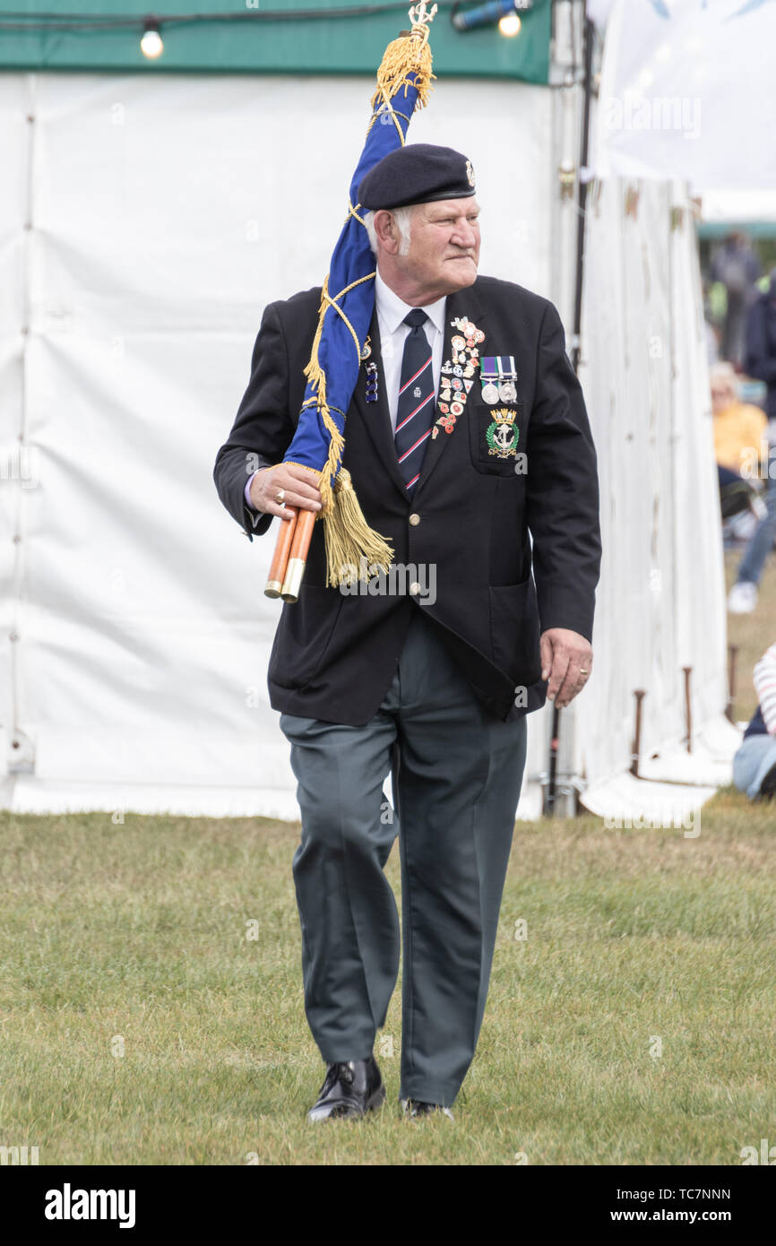 Un veterano de las fuerzas armadas luciendo medallas portando una bandera durante el día-D 75 conmemoraciones en Portsmouth Foto de stock