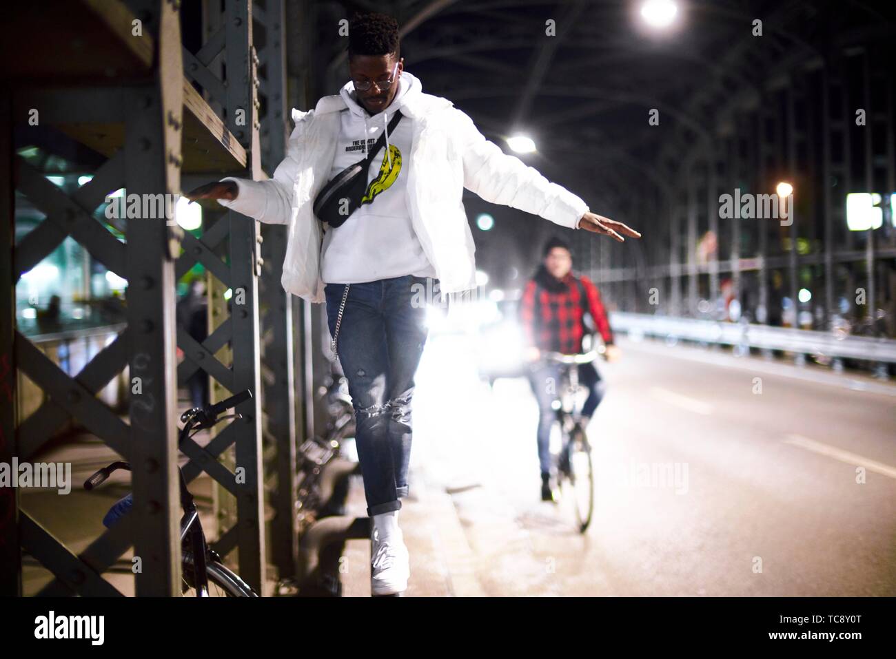 Joven equilibrio sobre construcción de puente de metal, Hacker Haccurbrücke bridge, en la noche en la ciudad, junto a la calle, conductor de bicicletas, en Munich, Alemania. Foto de stock