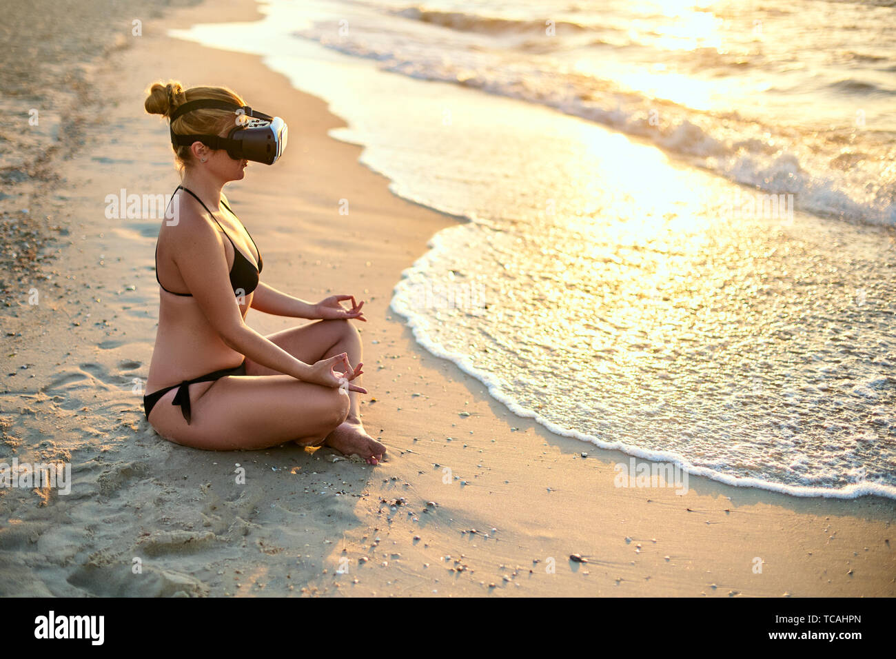 Mujer con gafas VR padmasana haciendo yoga en la playa por la mañana. Chica  utilizando la realidad virtual para la inmersión profunda para sentirse a  sí misma en el mar Fotografía de
