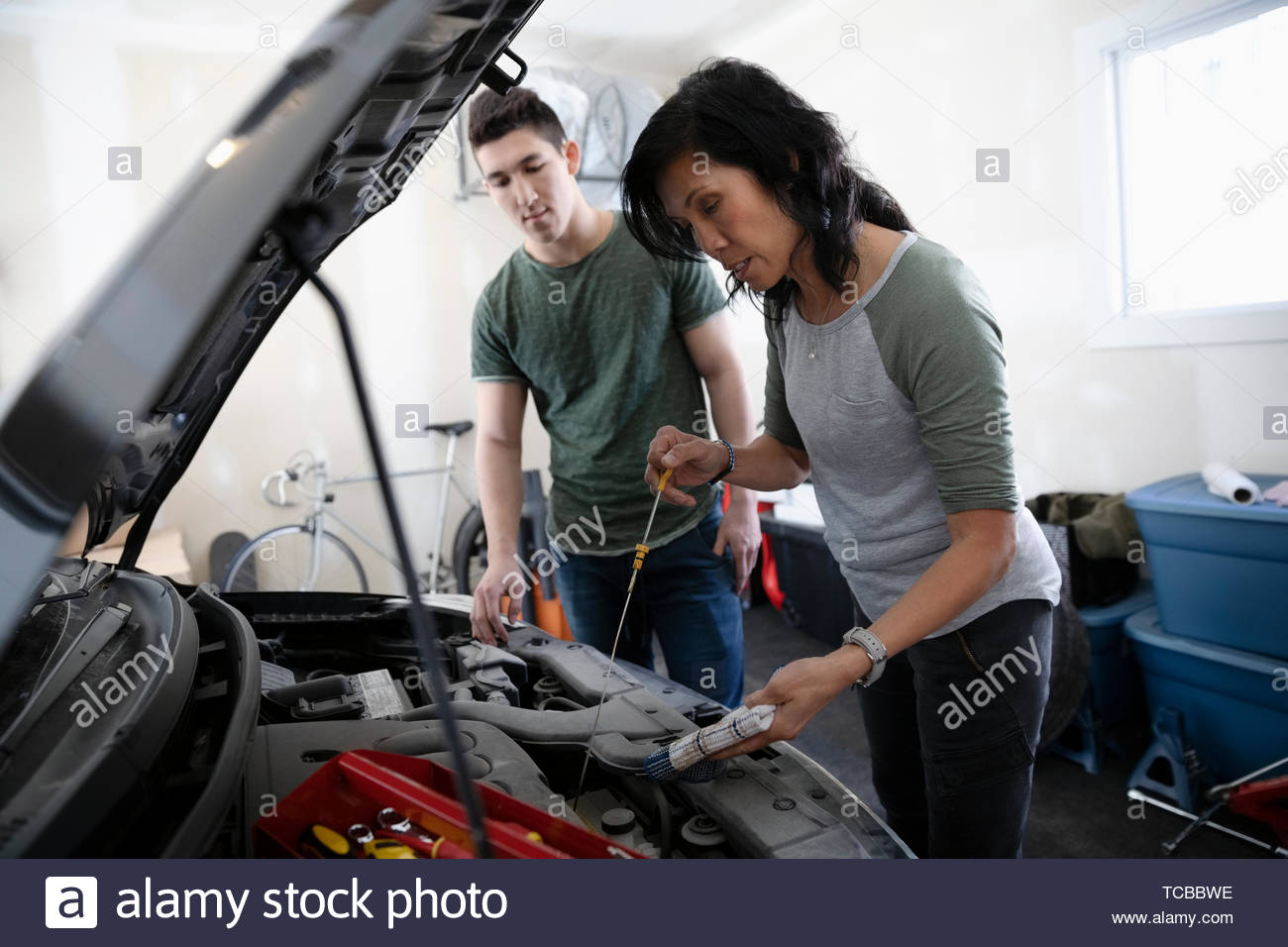 Hijo de madre enseñar cómo cambiar aceite bajo el capó del automóvil en el garaje Foto de stock