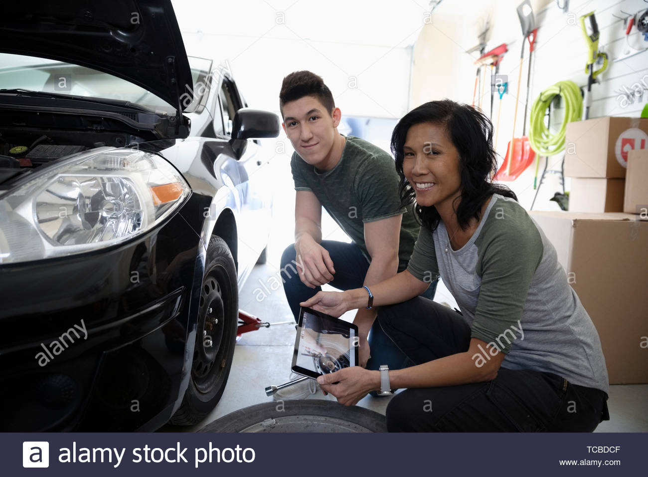 Retrato feliz madre e hijo con la tableta digital aprender a cambiar los neumáticos de coche en el garaje Foto de stock