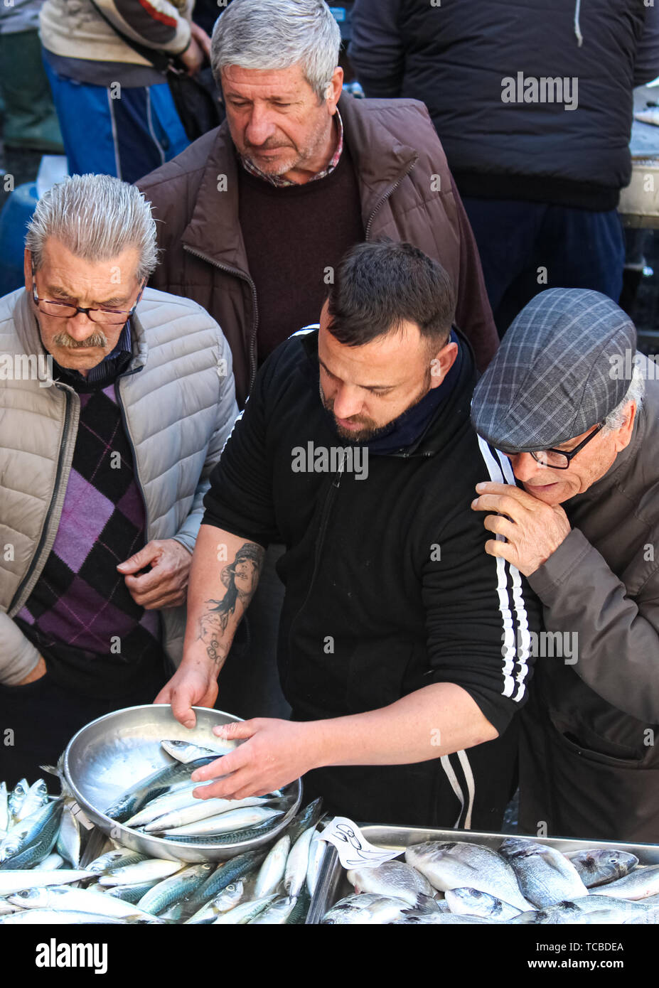 En Catania, Sicilia, Italia - 10 Abr 2019: Pescadería, la venta de pescado fresco en el tradicional mercado de pescado. Hombre mayor, exigente, le está tocando y dar instrucciones. Escena del mercado típico italiano. Foto de stock