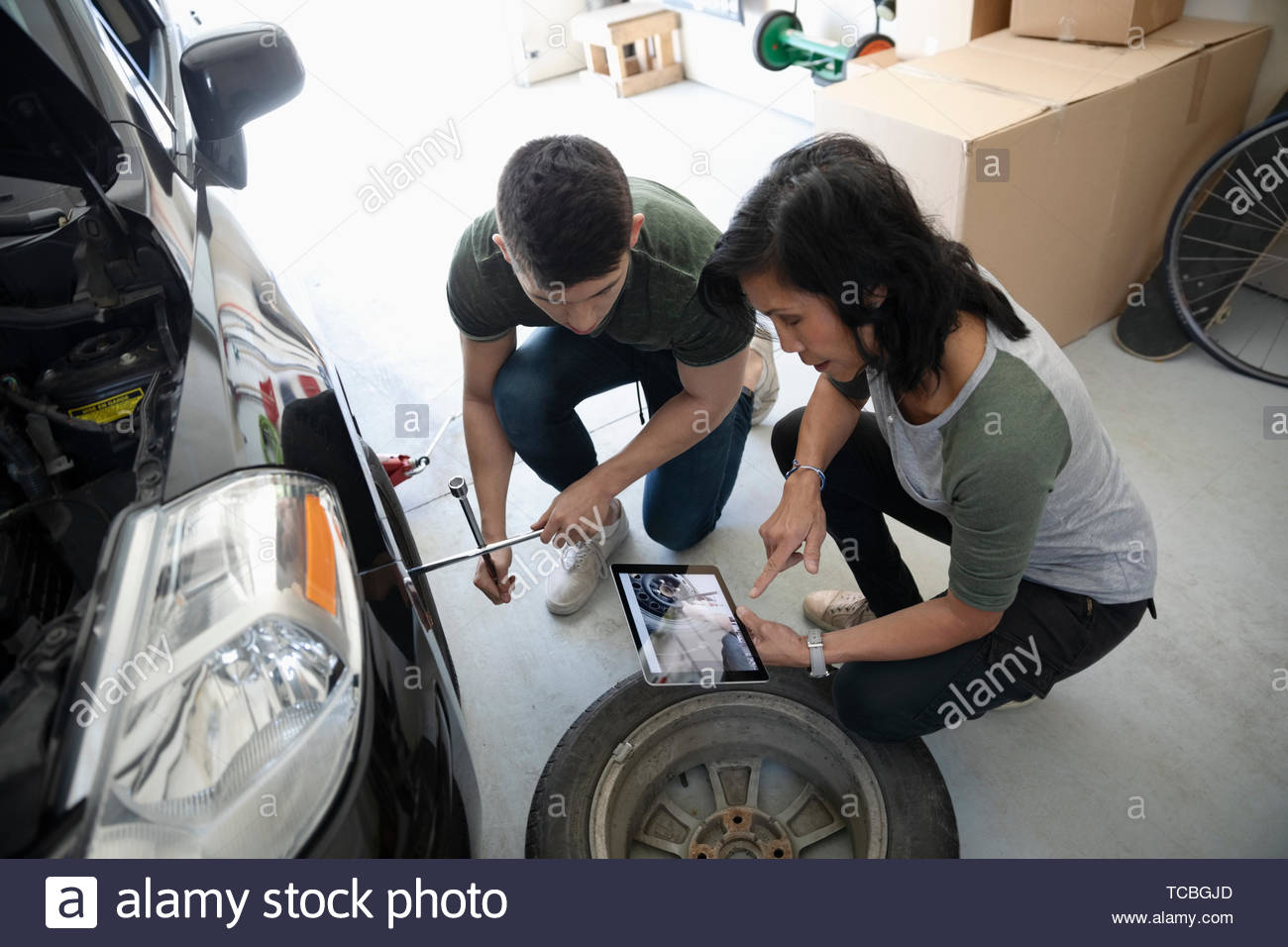 Madre e hijo con la tableta digital aprender a cambiar los neumáticos de coche en el garaje Foto de stock