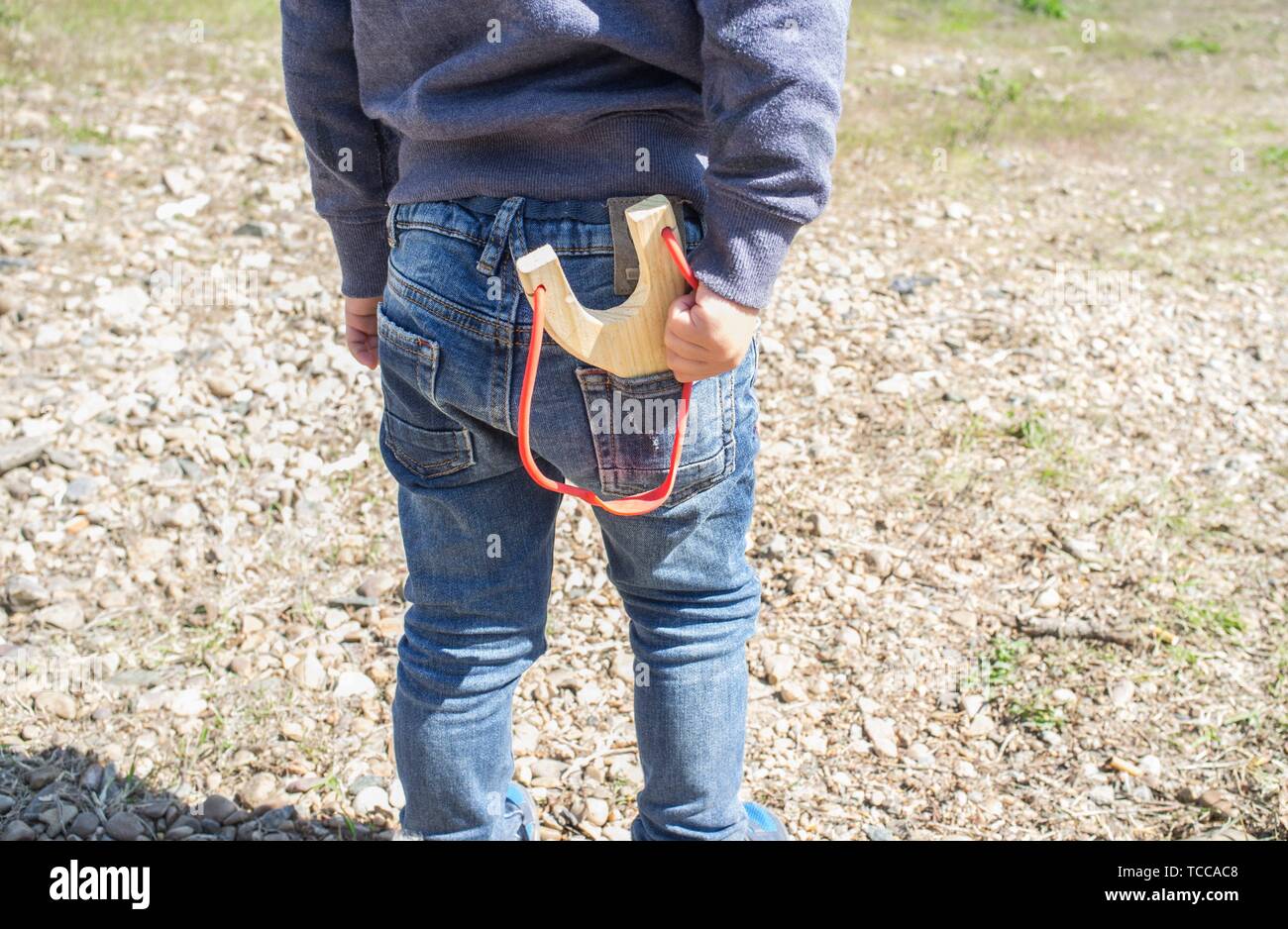 3 años chico con tirachinas en el bolsillo de los pantalones vaqueros. Él está preparando el próximo disparo. Foto de stock