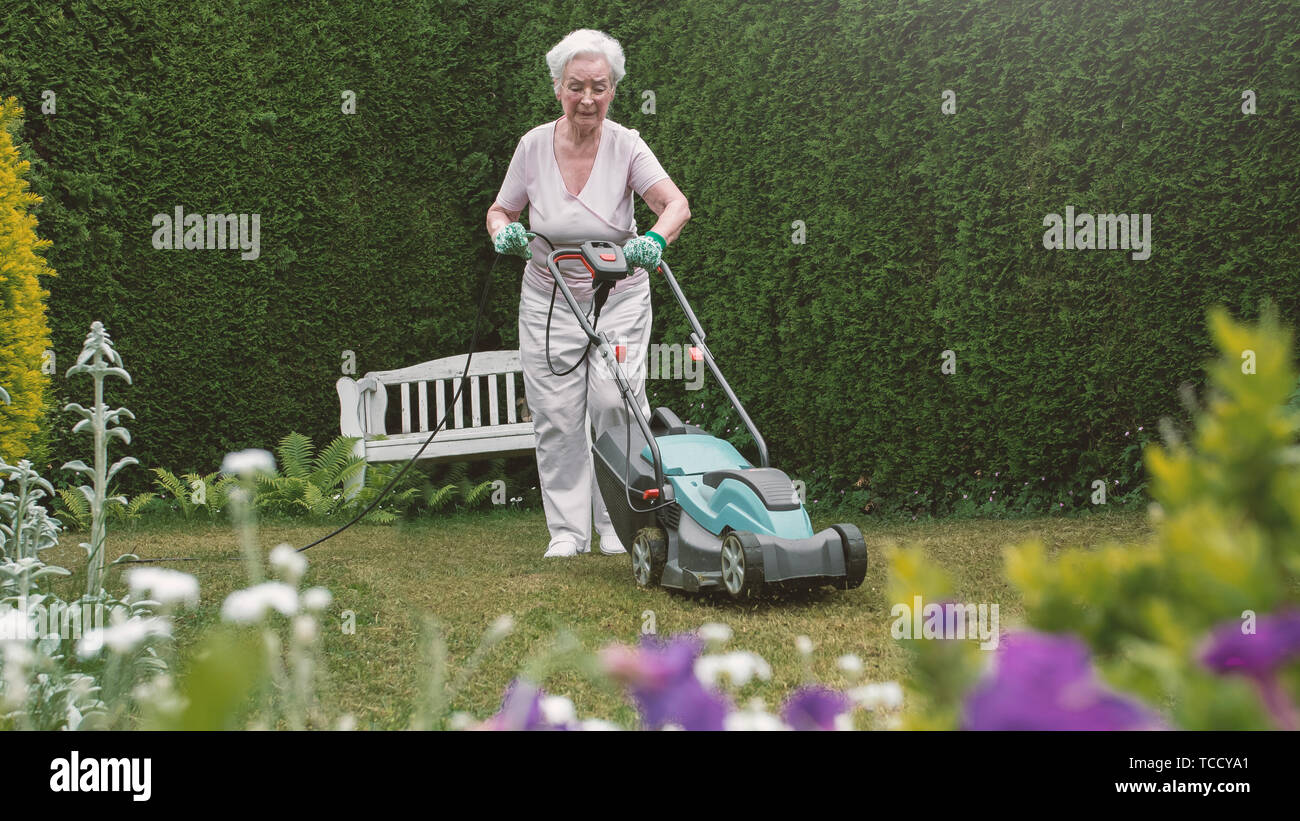 Senior mujer trabajando en el jardín con la segadora Foto de stock