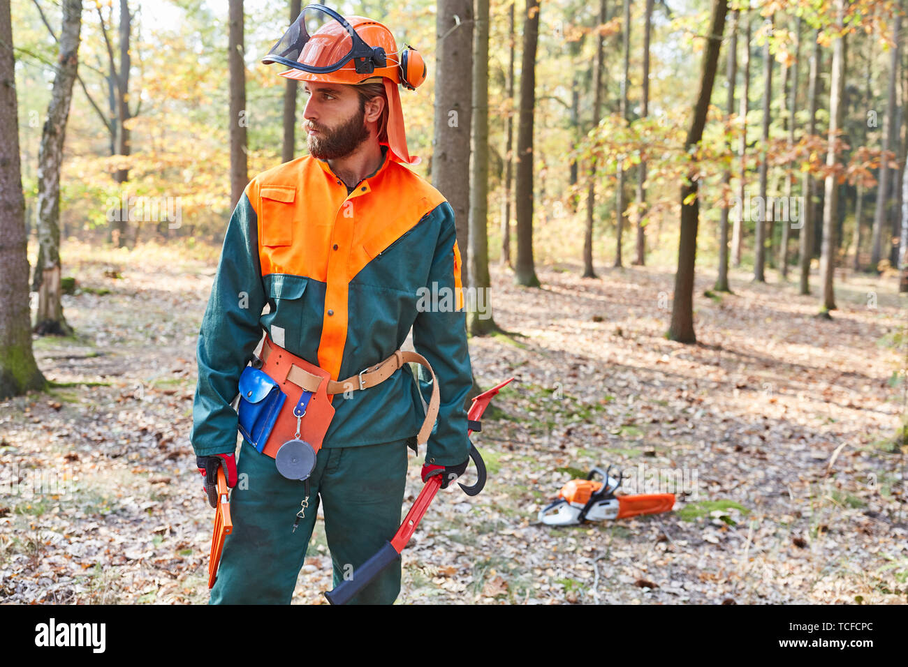 Le ador o trabajador forestal en ropa protectora y con motosierra