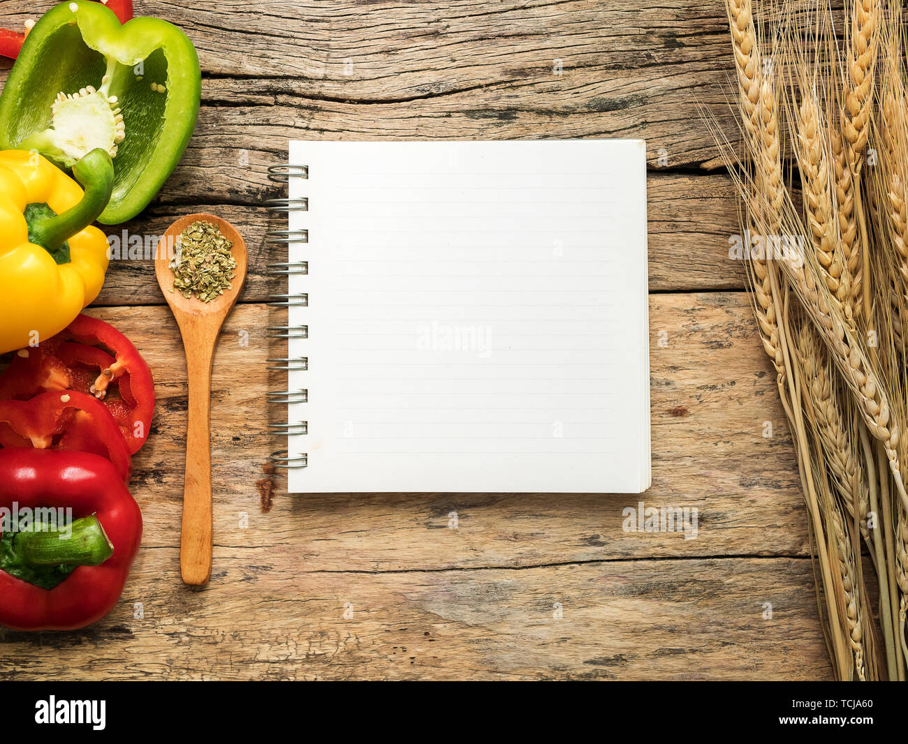 Plano de laicos en blanco del libro de cocina de recetas y utensilios con  hierbas y pimiento colorido sobre fondo de madera. Vista superior con  espacio de copia una receta de alimentos