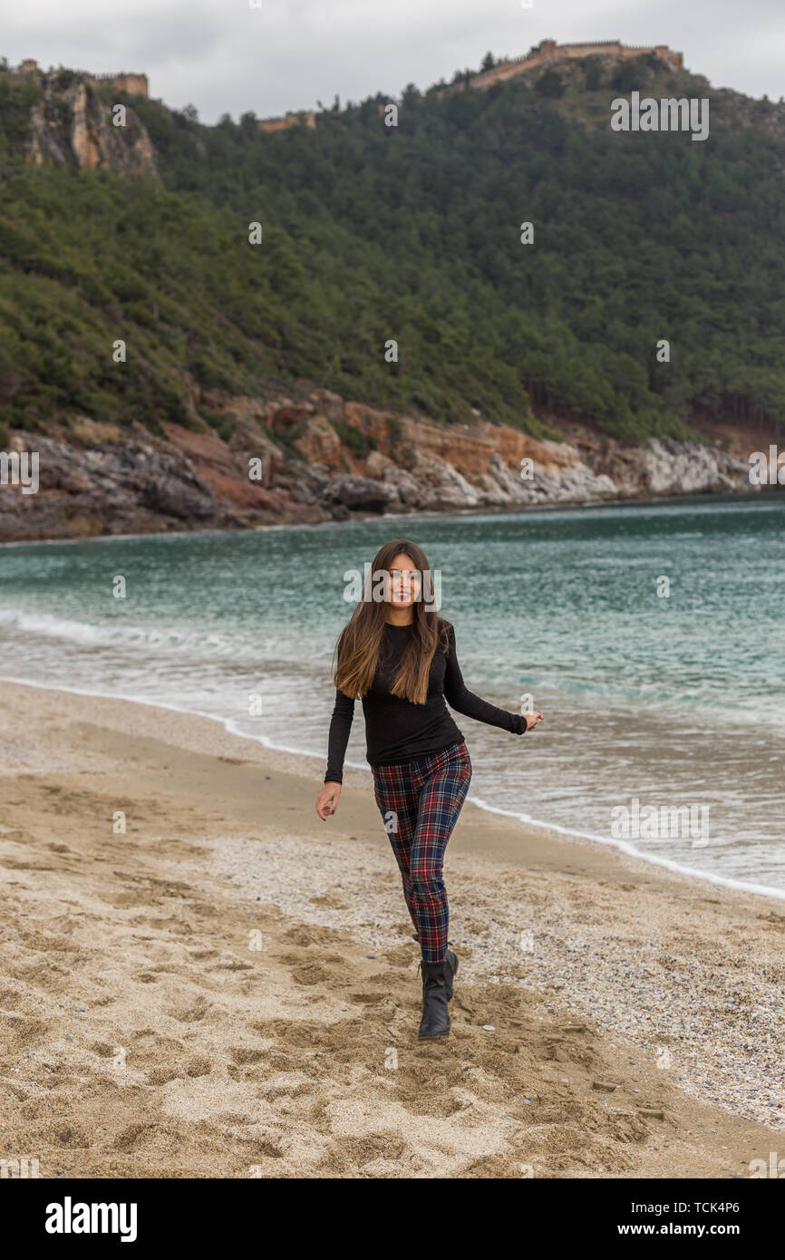 Colocar hermosas mujeres vistiendo pantalones suéter negro y comprobar ejecutando a playa de invierno Foto de stock