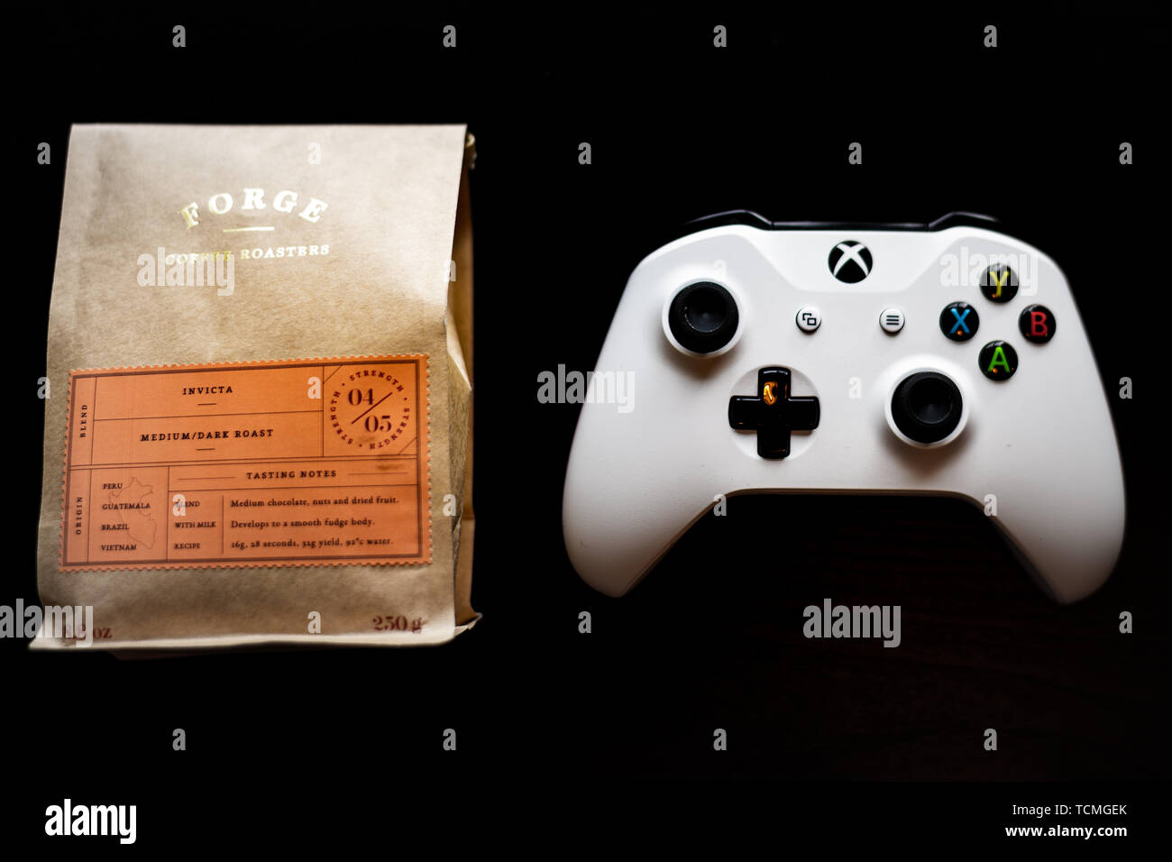 Controlador de juegos Xbox uno sentado junto a una bolsa de café molido contra un fondo negro oscuro Foto de stock
