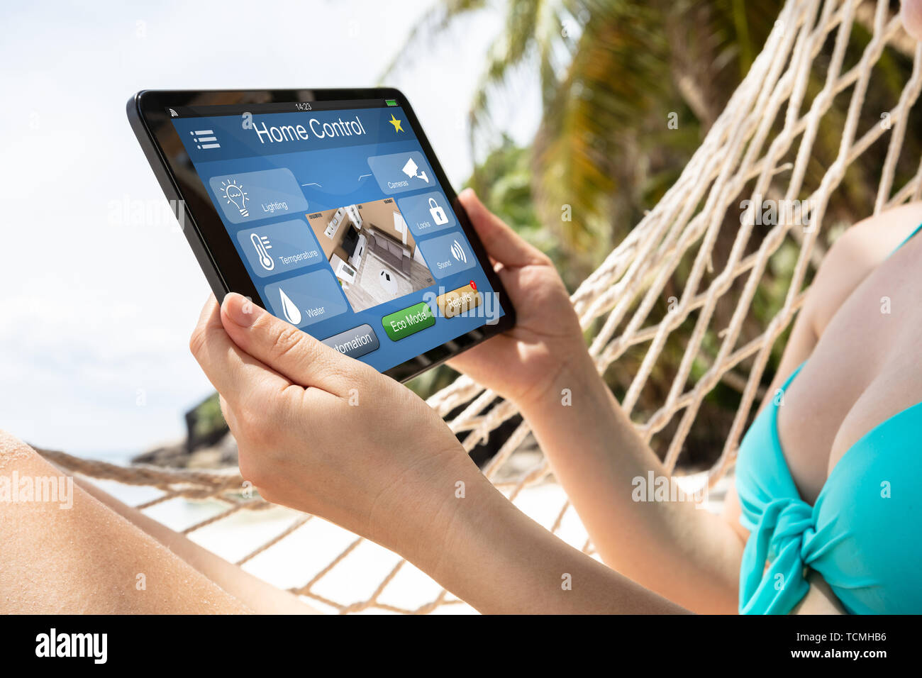 Mujer joven tumbado en una hamaca con la automatización inteligente en el hogar sobre la tableta digital en Playa Foto de stock