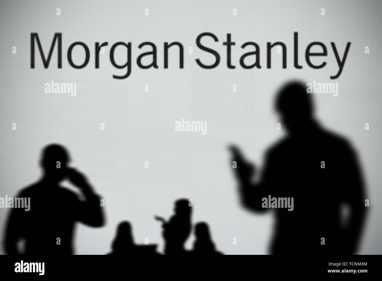 El logotipo de Morgan Stanley es visto en una pantalla LED en el fondo mientras una silueta persona utiliza un smartphone en primer plano (uso Editorial solamente) Foto de stock