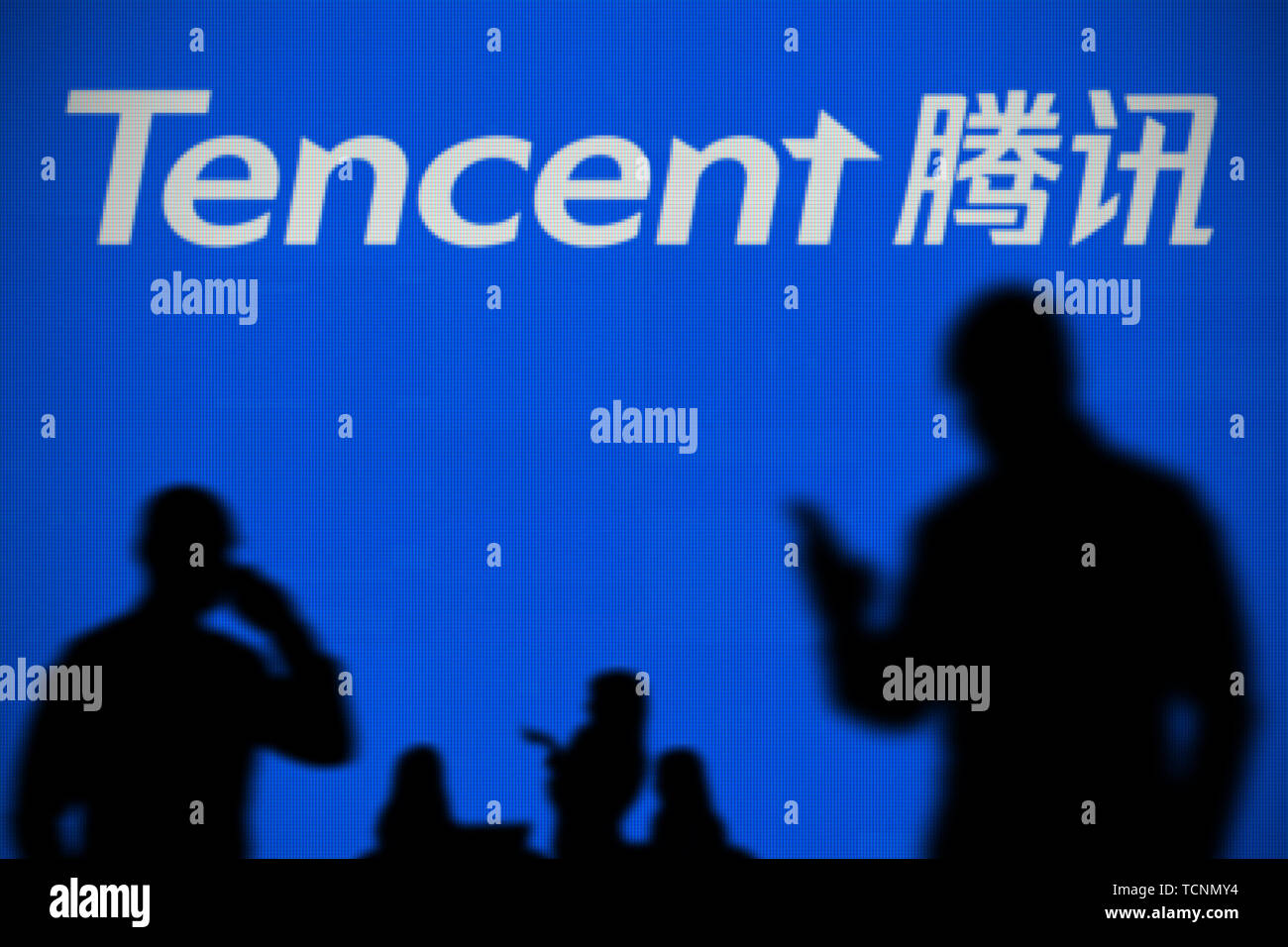 El Tencent logo es visto en una pantalla LED en el fondo mientras una silueta persona utiliza un smartphone en primer plano (uso Editorial solamente) Foto de stock