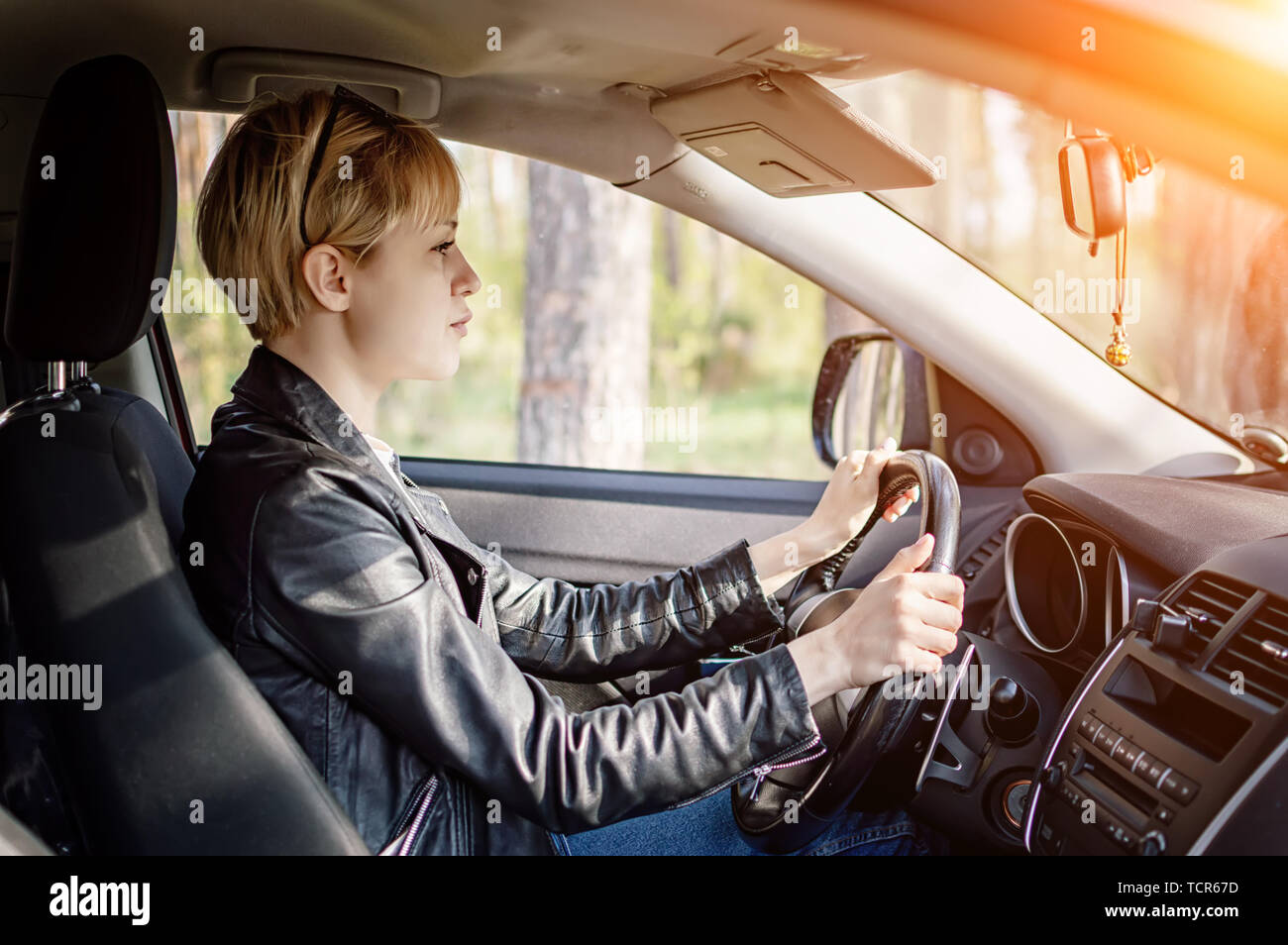 Hermosa chica con un corte de pelo corto y una chaqueta negra detrás del  volante de un auto. El cabello corto Fotografía de stock - Alamy