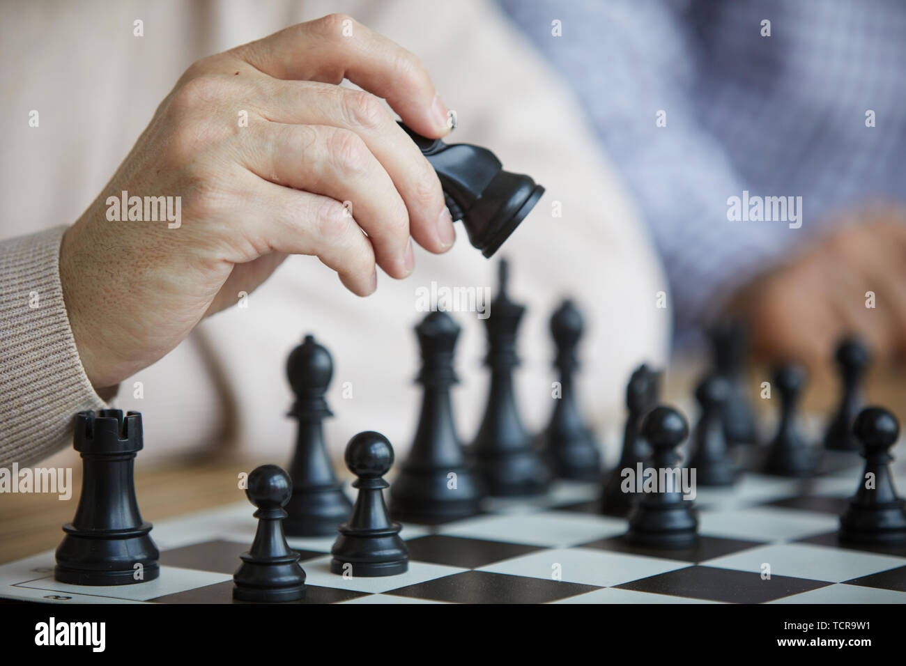Arrugada mano de antiguo jugador de ajedrez en beige suéter negro moviendo  la figura de ajedrez en un tablero de ajedrez Fotografía de stock - Alamy