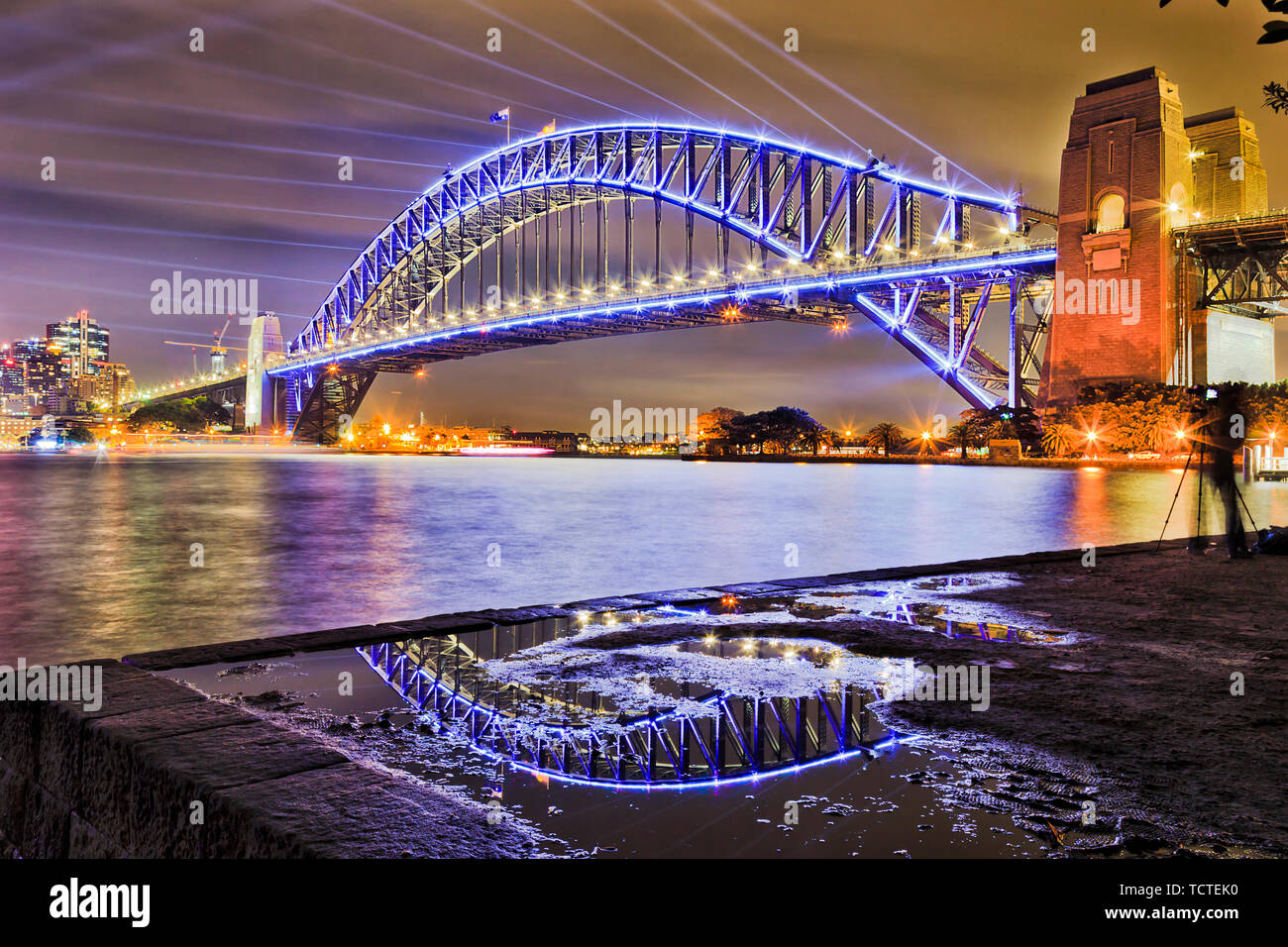 Arco de acero masivo del Sydney Harbour Bridge en Sydney Harbour reflejando  en el charco con haces de láser en color azul cielo oscuro en vivo show de  luces de Sydney Fotografía