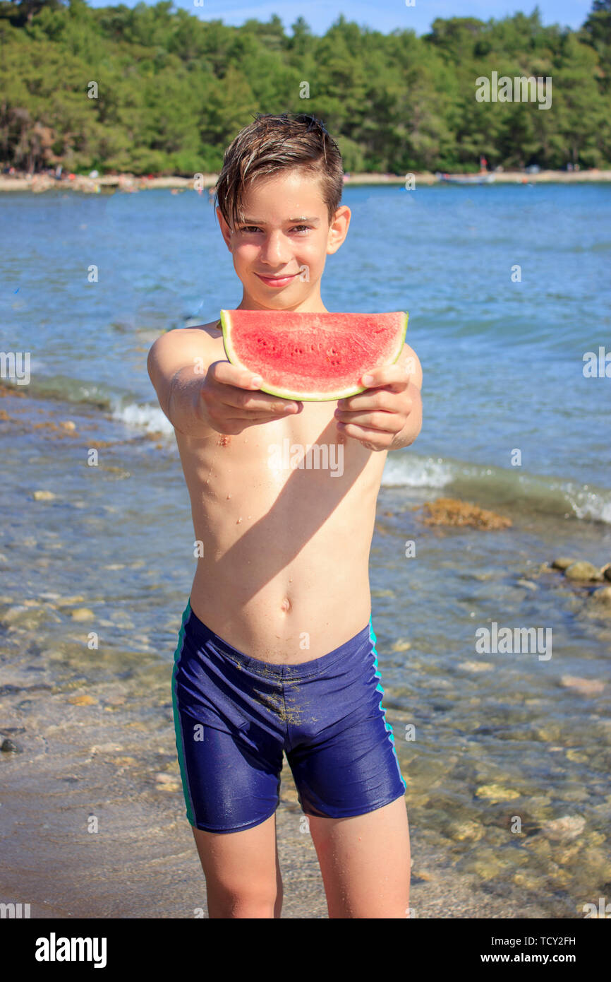 Lindo adolescente muchacho sostiene la rebanada de sandía en la playa junto  al mar Fotografía de stock - Alamy