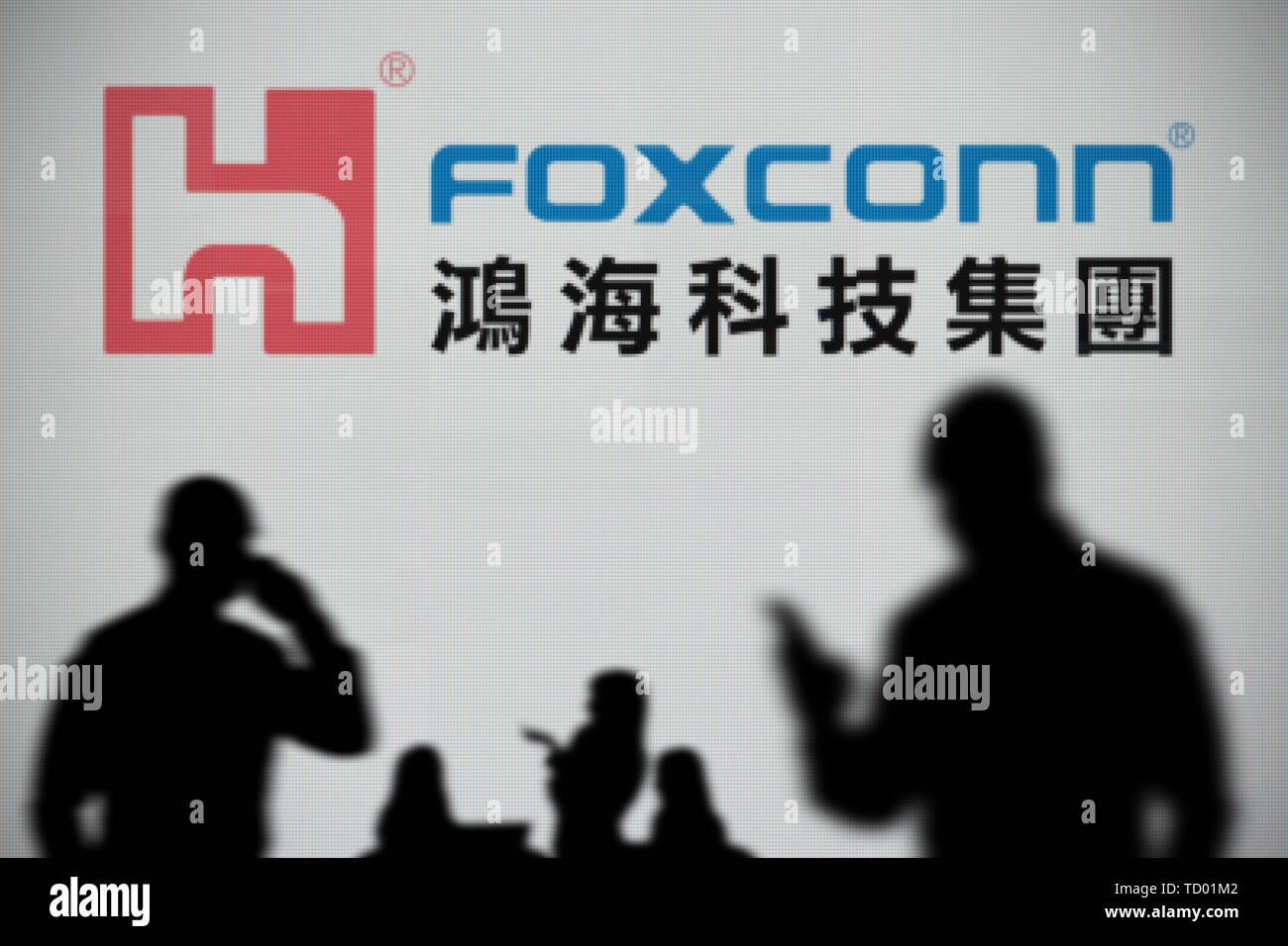 El logotipo de Foxconn es visto en una pantalla LED en el fondo mientras una silueta persona utiliza un smartphone en primer plano (uso Editorial solamente) Foto de stock