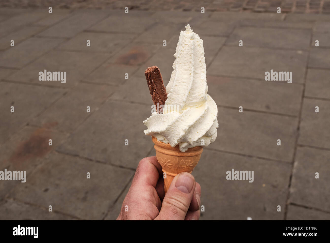 Primer plano de un hombre azotado mano sosteniendo un helado de crema con copos de chocolate que sobresalen del lado, aisladas contra un fondo liso Foto de stock
