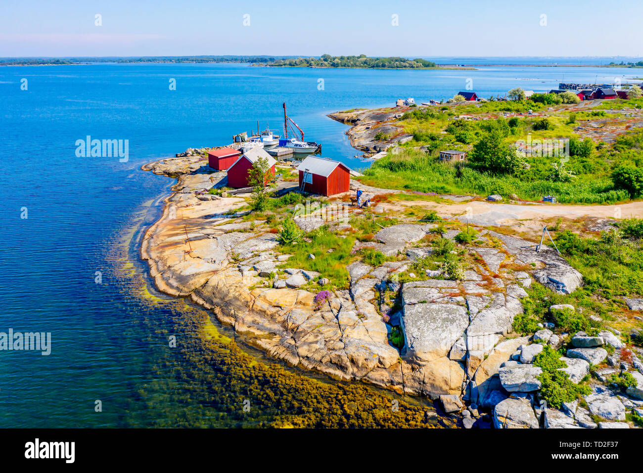 Hasslo, Suecia - Junio 3, 2019: Rojo cobertizos de pesca y un pequeño puerto en el precioso paisaje costero. La gente, el perro y el trolley visible por los cobertizos. Foto de stock