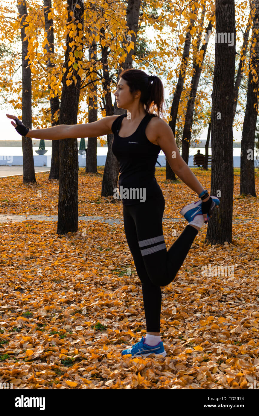 Jabarovsk, Rusia - 07 Oct, una mujer en ropa deportiva haciendo deportivos en la naturaleza frente a la puesta del sol y el río Amur, AMA Fotografía de stock -