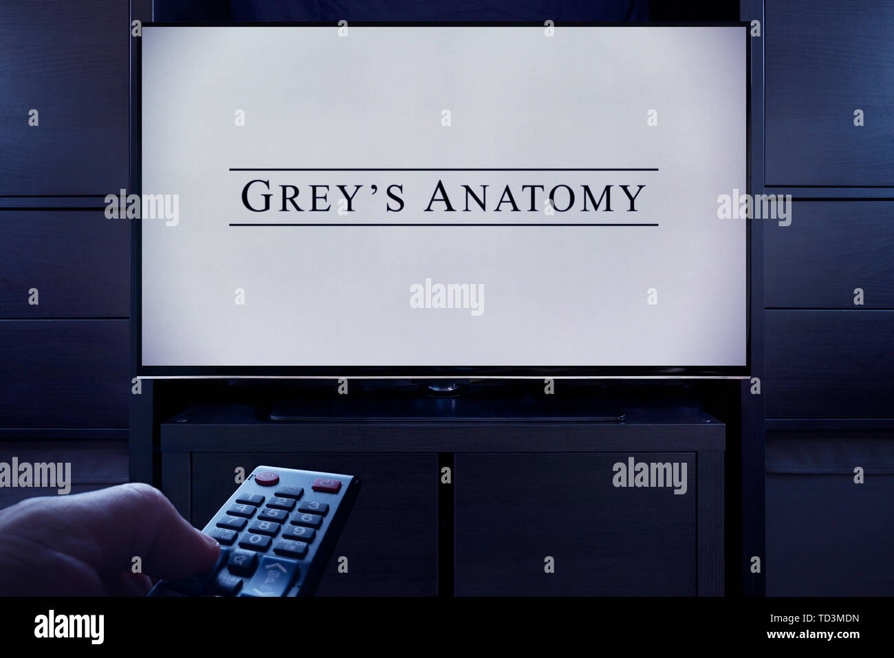 Un hombre apunta un control remoto de la televisión en la televisión que muestra la Anatomía de Gray's pantalla de título principal (sólo para uso editorial). Foto de stock