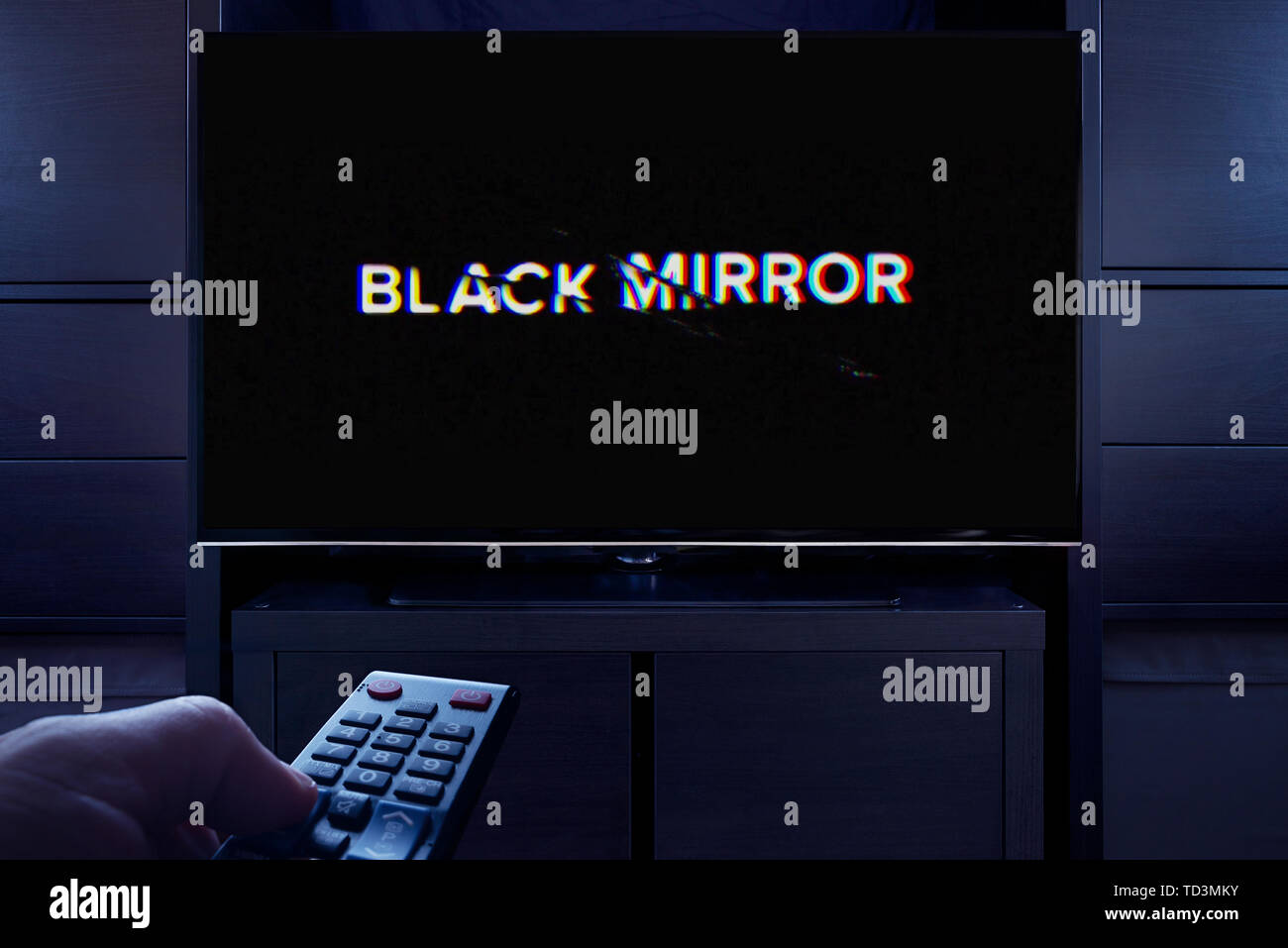Un hombre apunta un control remoto de la televisión en la televisión que muestra la pantalla de título principal Negro espejo (uso Editorial solamente). Foto de stock
