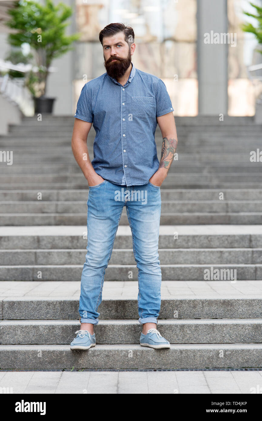 En el amor con jeans. El hombre barbado hipster fashion modelo denim  desgaste ropa fondo urbano escaleras. Caminar en el centro de la ciudad.  Seguros de guy llevar vaqueros pantalones vaqueros y