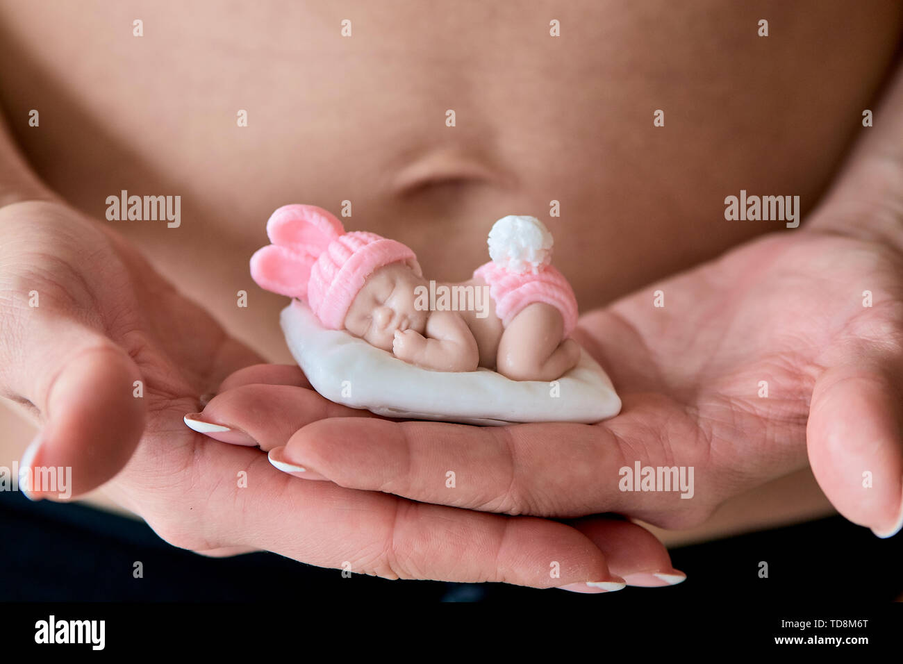 Jóvenes embarazadas woomen posee una figurilla de jabón en la forma de un  bebé recién nacido niña delante de su vientre en sus palmas sobre un fondo  blanco. Close-up Fotografía de stock -