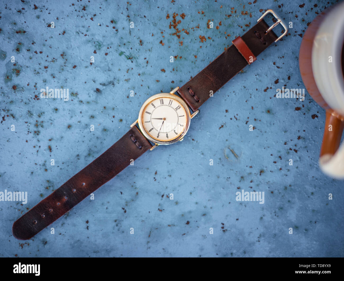 Vintage reloj de pulsera en el rústico banco de metal azul sugiriendo el tiempo es 07.00, una taza de café en el borde del bastidor. Foto de stock