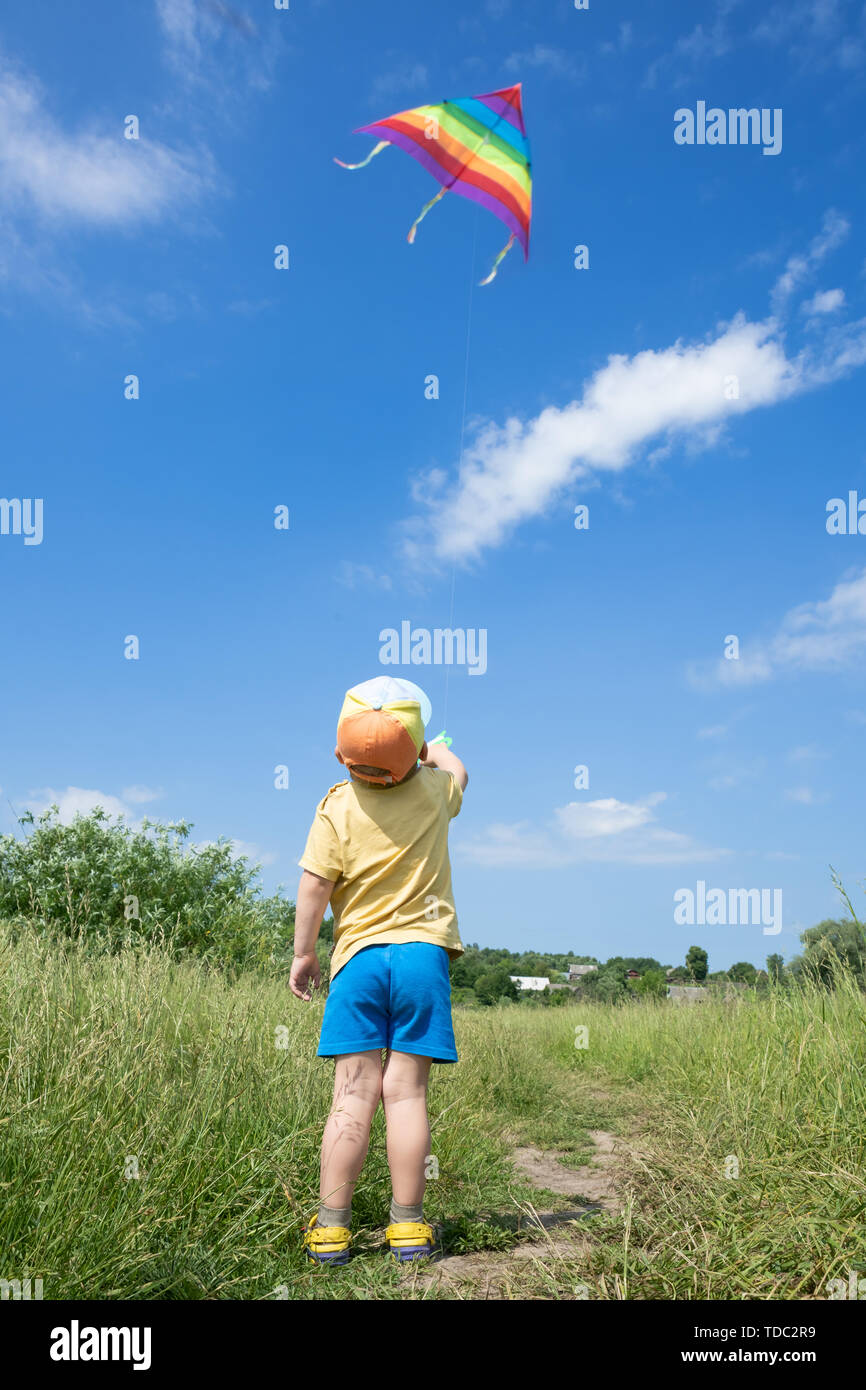 Little Boy lanza coloridas cometas en el cielo azul Foto de stock