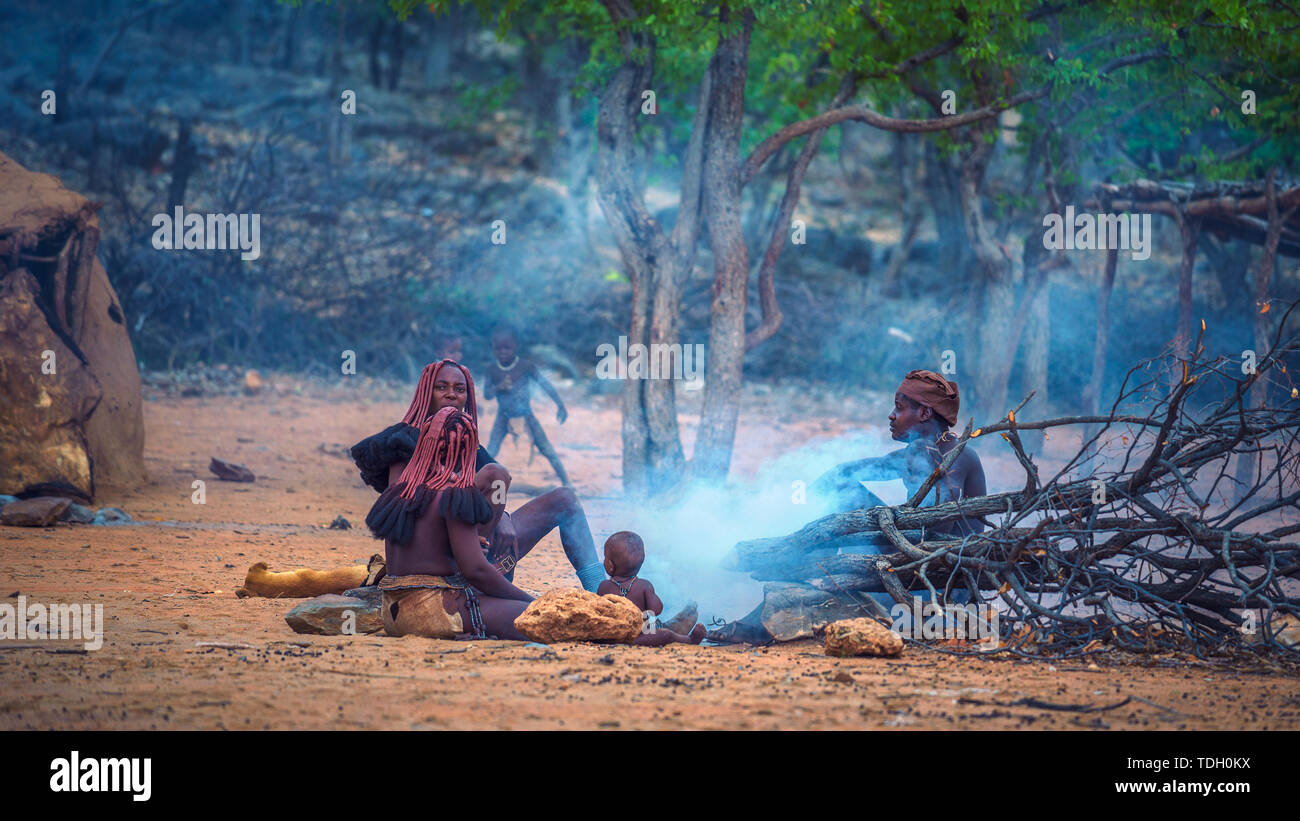 La gente de la tribu Himba sentados alrededor del fuego en su aldea Foto de stock
