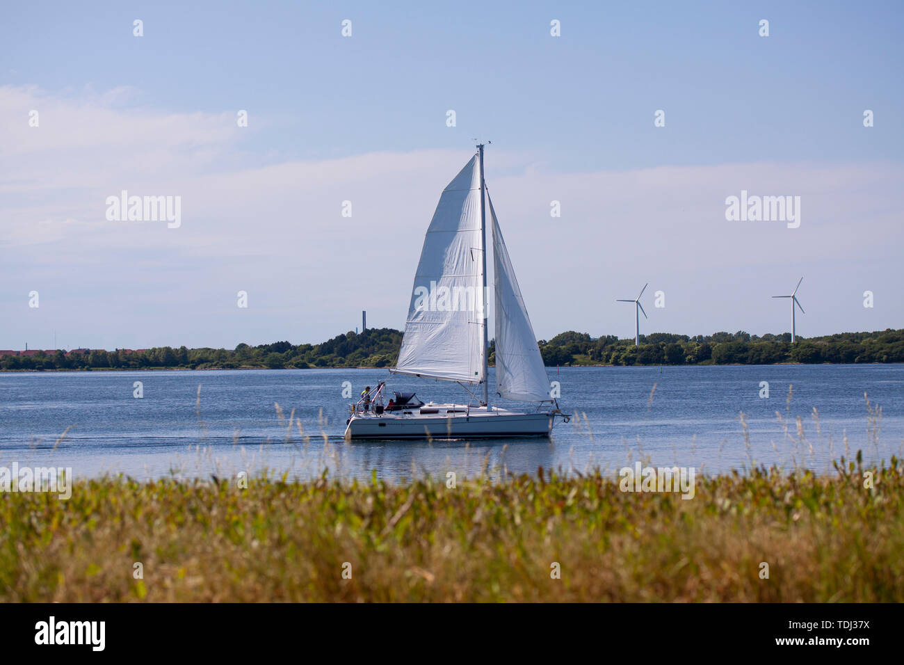 Velero para navegar en un río en un día soleado con turbinas de viento en el fondo. Copenhague, Dinamarca - 14 de junio de 2019. Foto de stock