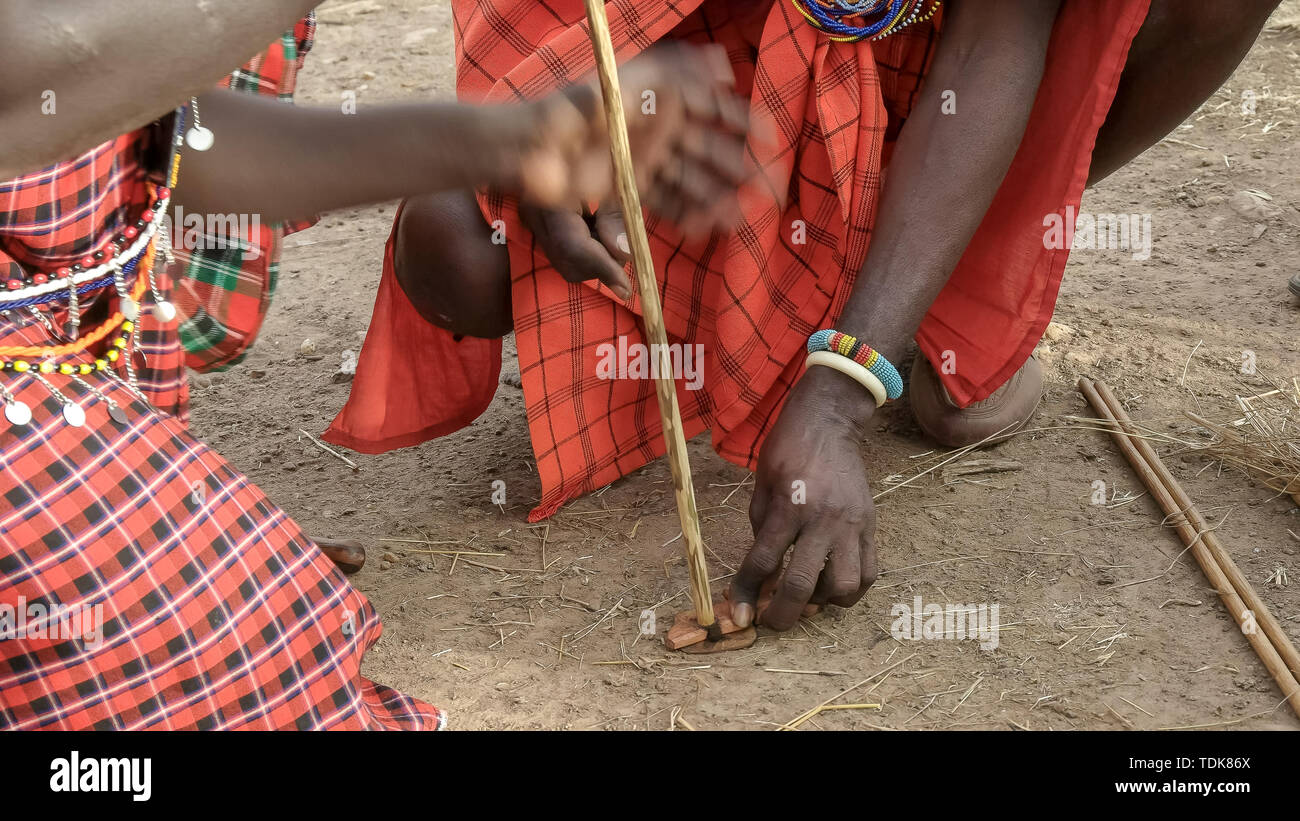 Dos hombres Masai, use un taladro de mano tradicional para empezar un fuego sin cerillas en una manyatta en Kenya Foto de stock