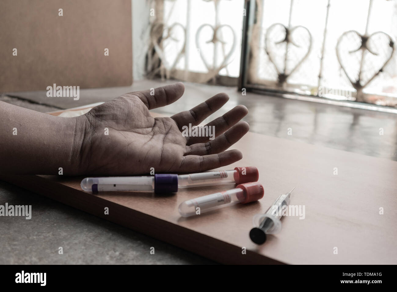 Drogadicto con jeringa de mano en el suelo con tubos de drogas Foto de stock