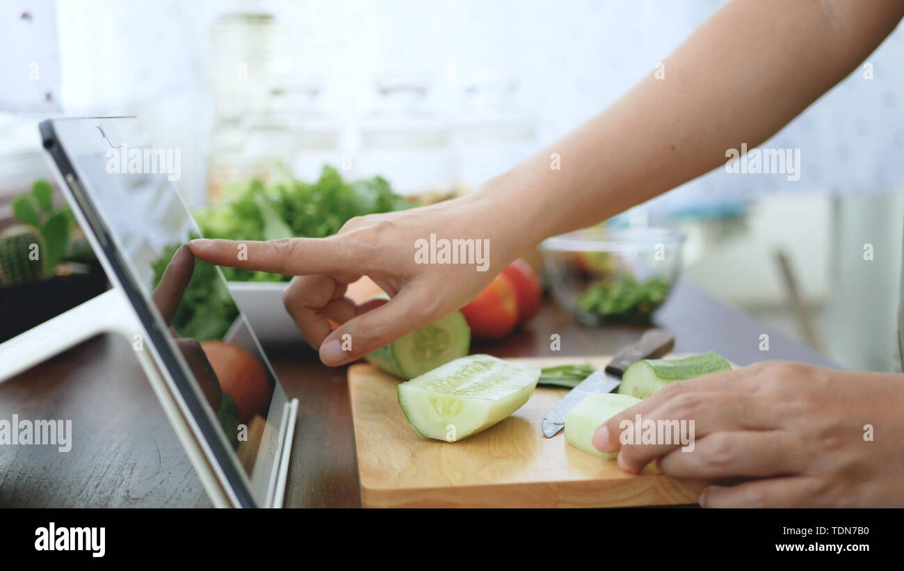 Mujer Asiática uso deslizar el dedo en la pantalla de tablet pc preparar los ingredientes para cocinar siga cocinando vídeo online en el sitio web. Cocinar el contenido en internet Foto de stock