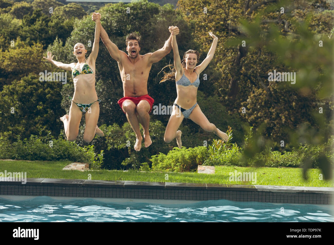 Amigos masculinos y femeninos saltando en la piscina en el patio Foto de stock