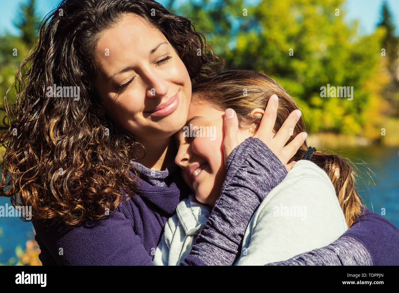 Una mamá abrazando a su hija fuertemente durante una excursión familiar en un parque de la ciudad en un cálido día de otoño; en Edmonton, Alberta, Canadá Foto de stock