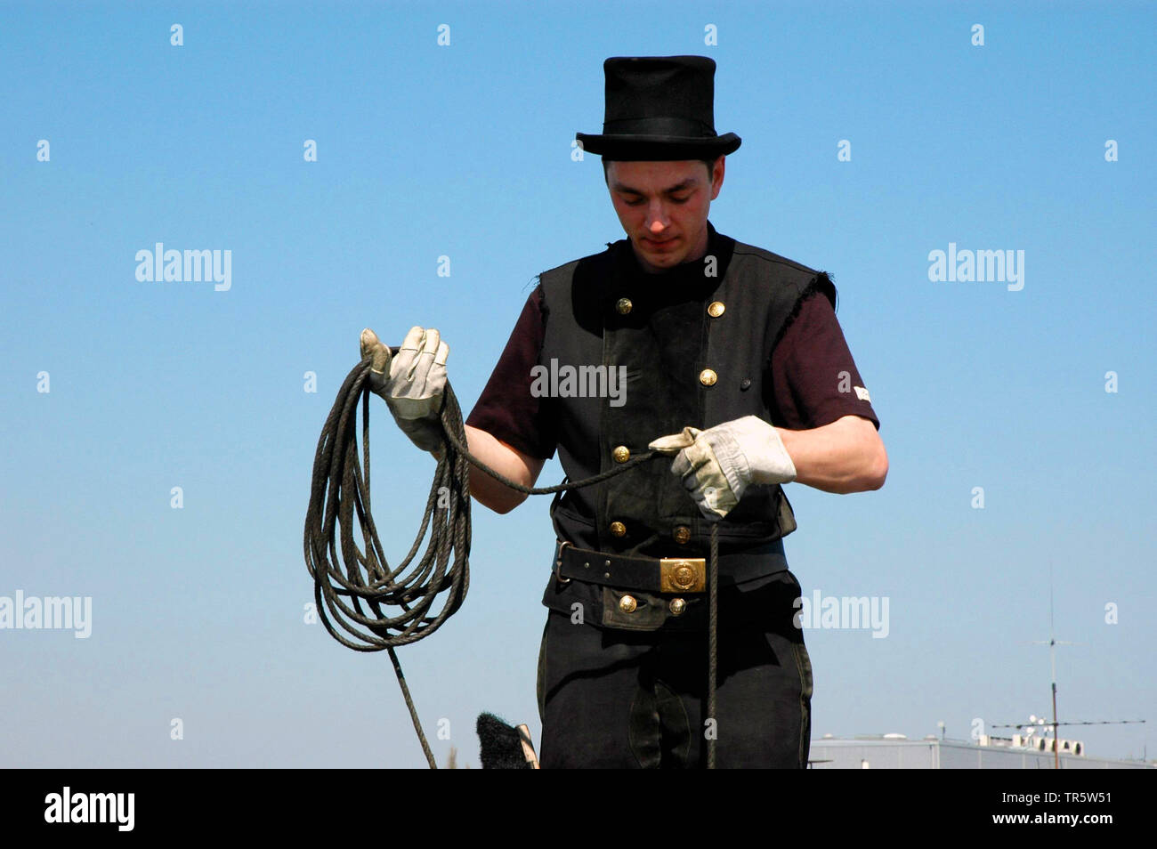 Un deshollinador en negro esmoquin y sombrero de abrigo--la ropa de trabajo  de su oficio--baja un cepillo para iniciar la limpieza de una chimenea de  ladrillo en California, Estados Unidos Fotografía de