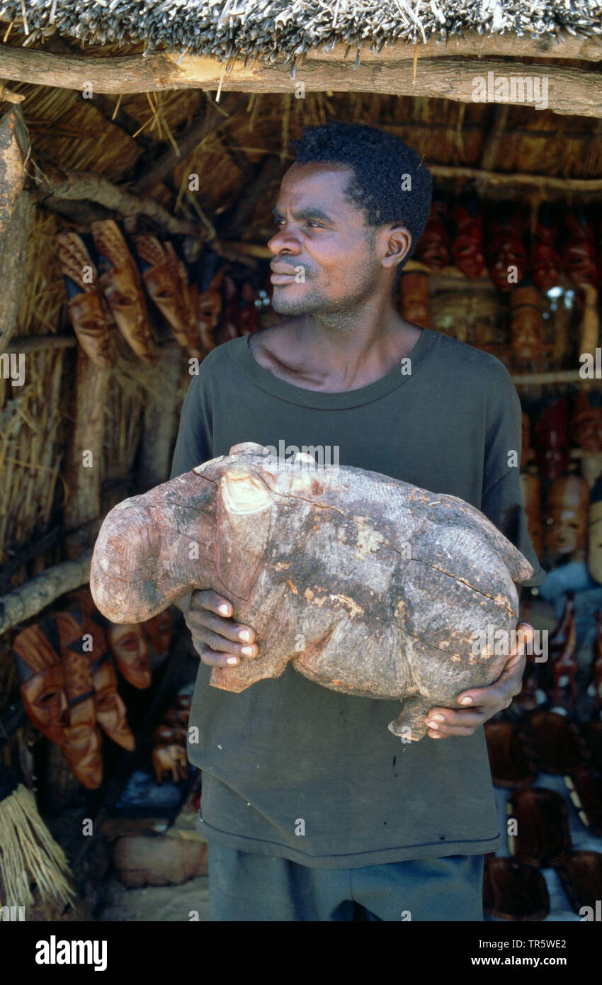 Hipopótamos, hipopótamos, hipopótamo común (Hippopotamus amphibius), el hombre con la escultura tallada de un hipopótamo, Namibia, Damaraland, Rundu Foto de stock