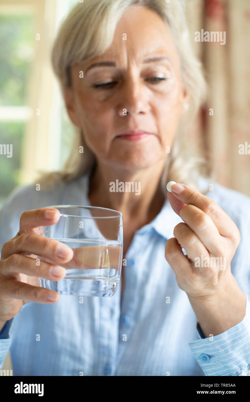 Mujer mayor tomando tabletas con un vaso de agua en casa. Foto de stock