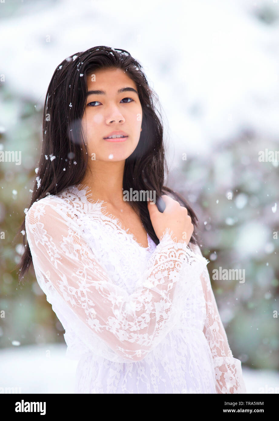 Birracial hermosa jovencita en blanco vestido encaje de pie afuera en invierno Foto de stock
