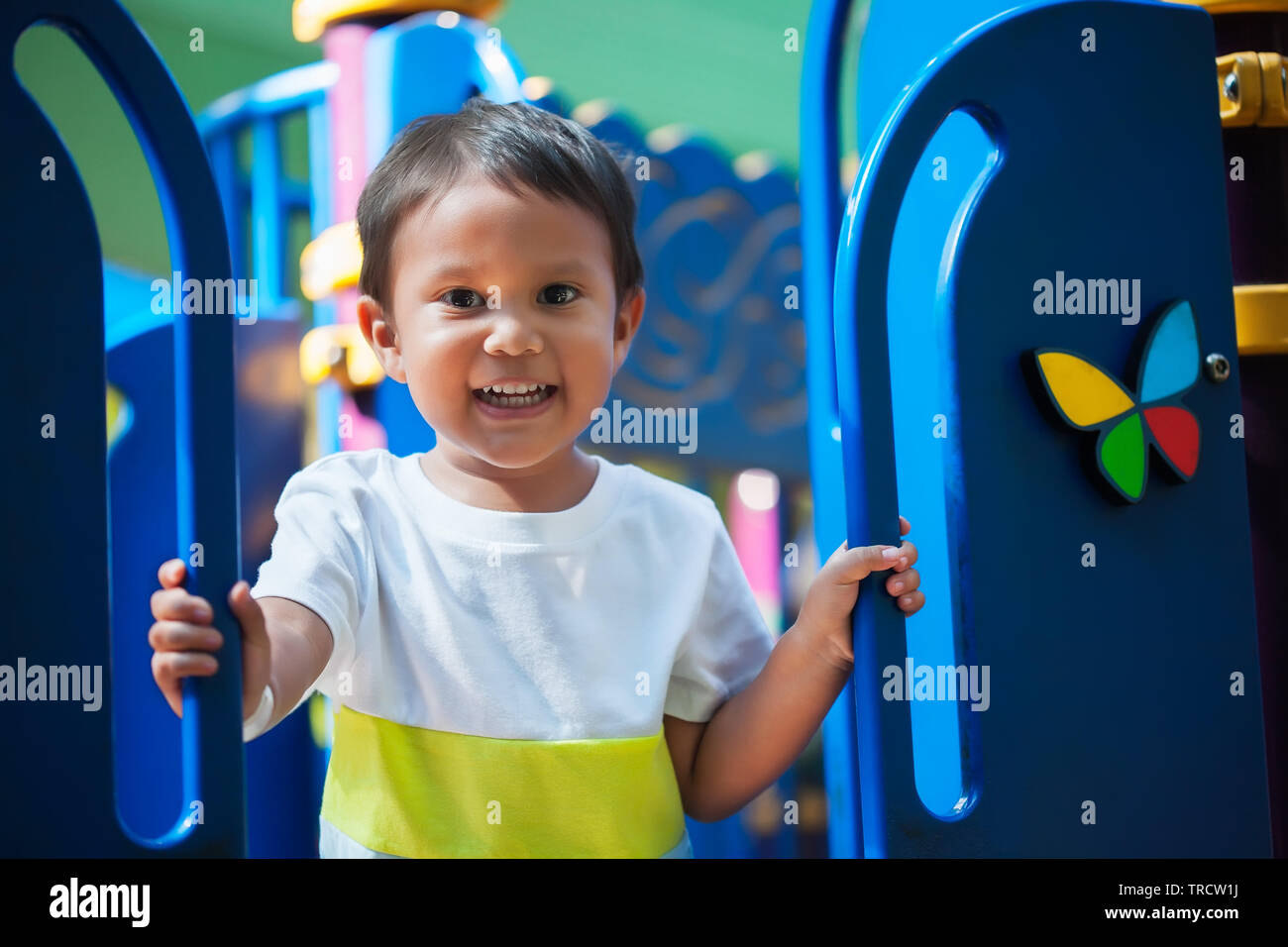 Sonriente joven niño sosteniendo desde un parque infantil gimnasia de selva con una mirada emocionada y lista para divertirse. Foto de stock