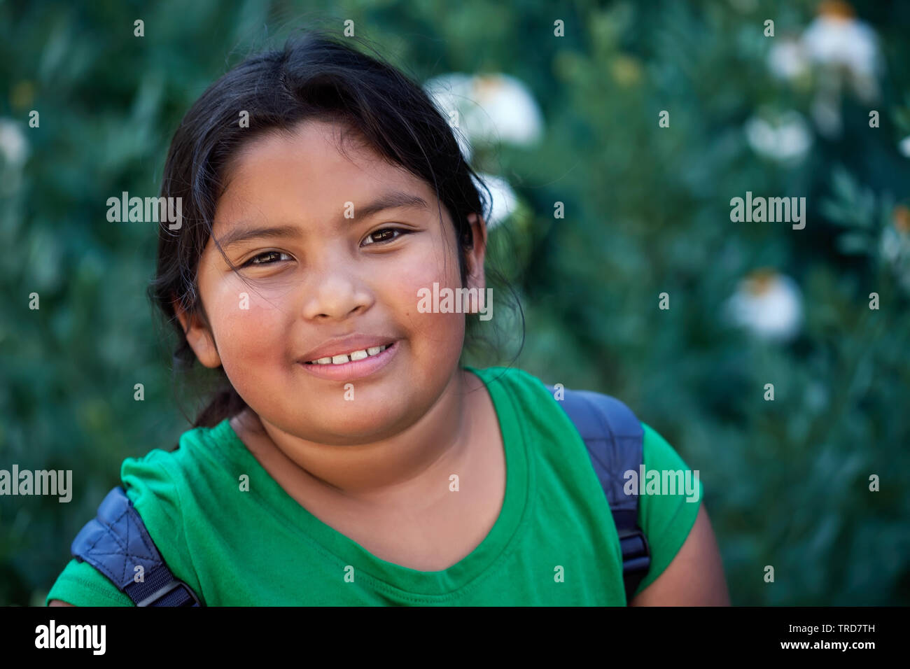 Lindo estudiante de primaria con mochila delante de flores verdes con una actitud positiva y de aspecto natural. Foto de stock