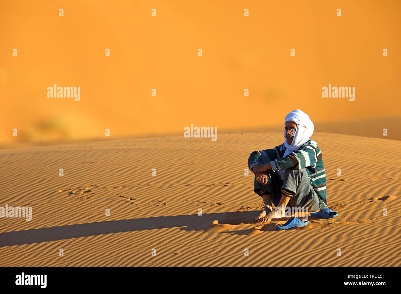 El bereber sentado en la arena del desierto, Marruecos, Merzouga, Erg Chebbi Foto de stock