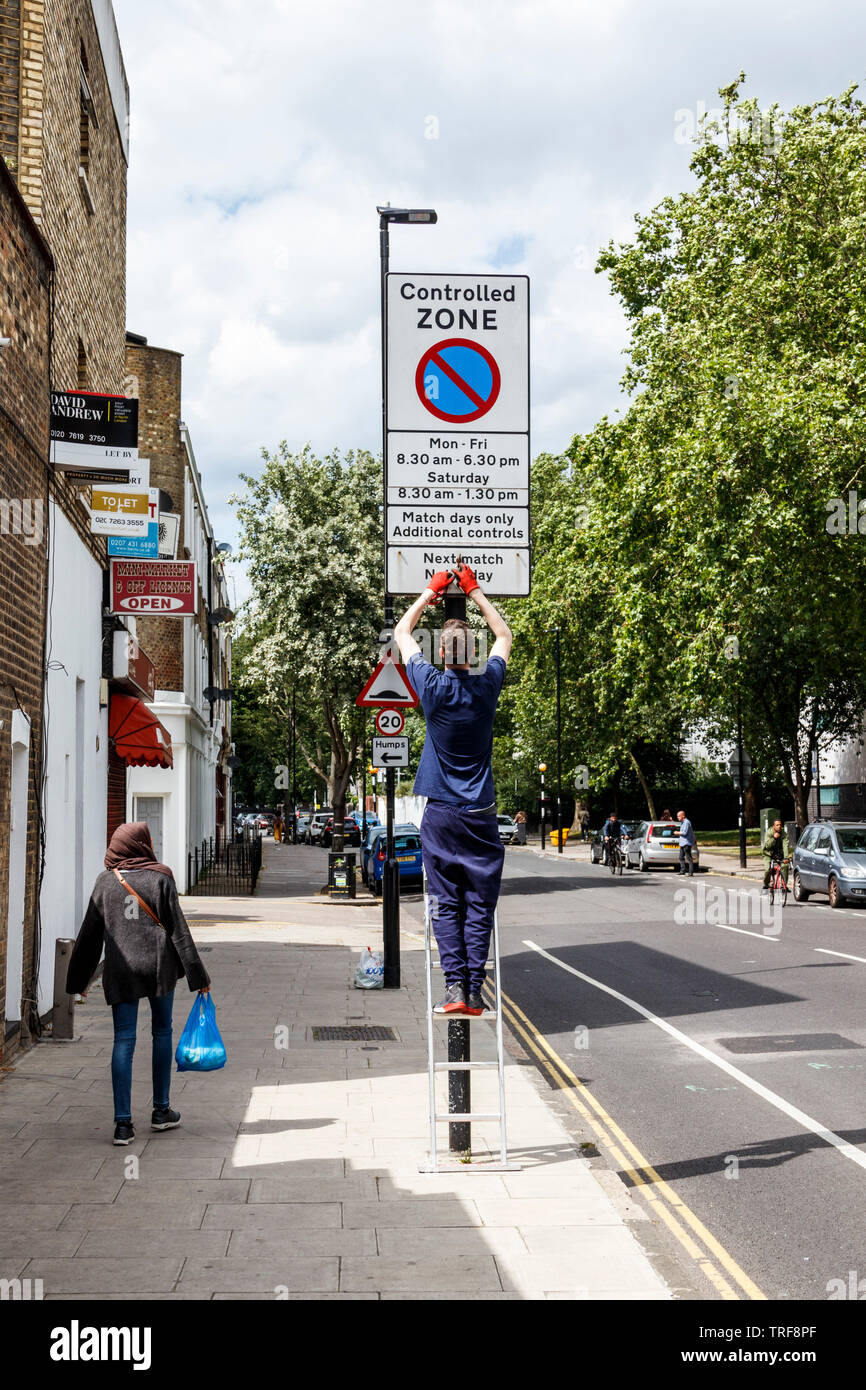 Un trabajador del Consejo arriba sumador al cambiar un match-día aviso de restricción de estacionamiento en Islington, Londres, Reino Unido. Foto de stock