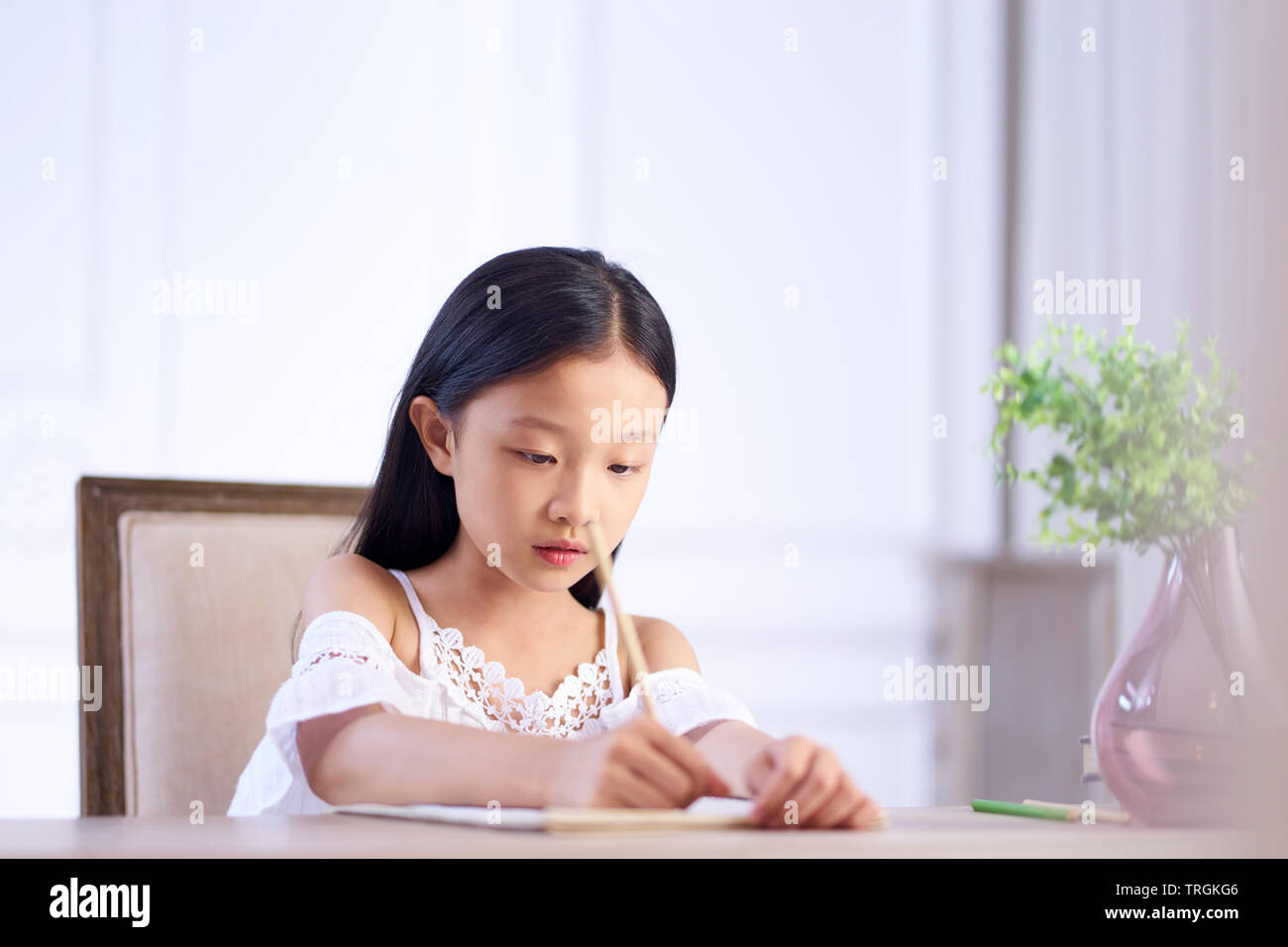 Bonita chica asiática con largo cabello negro sentado en el escritorio en su habitación escribiendo o dibujando sobre note book Foto de stock