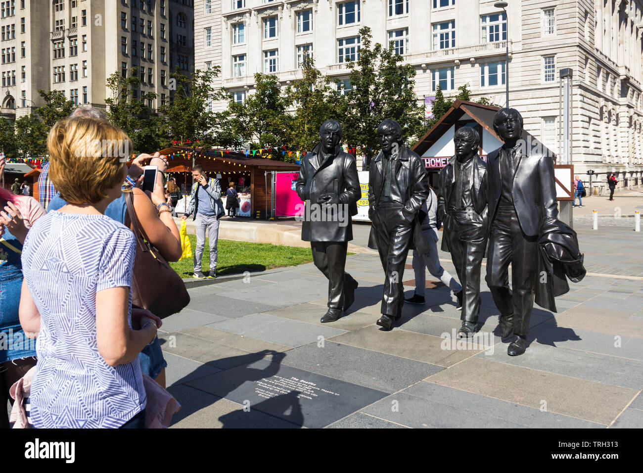 Los turistas viendo la estatua de los Beatles en Liverpool's Pier Head. La estatua fue descubierta en diciembre de 2015 y fue un regalo a la ciudad por el Cavern Club. Foto de stock