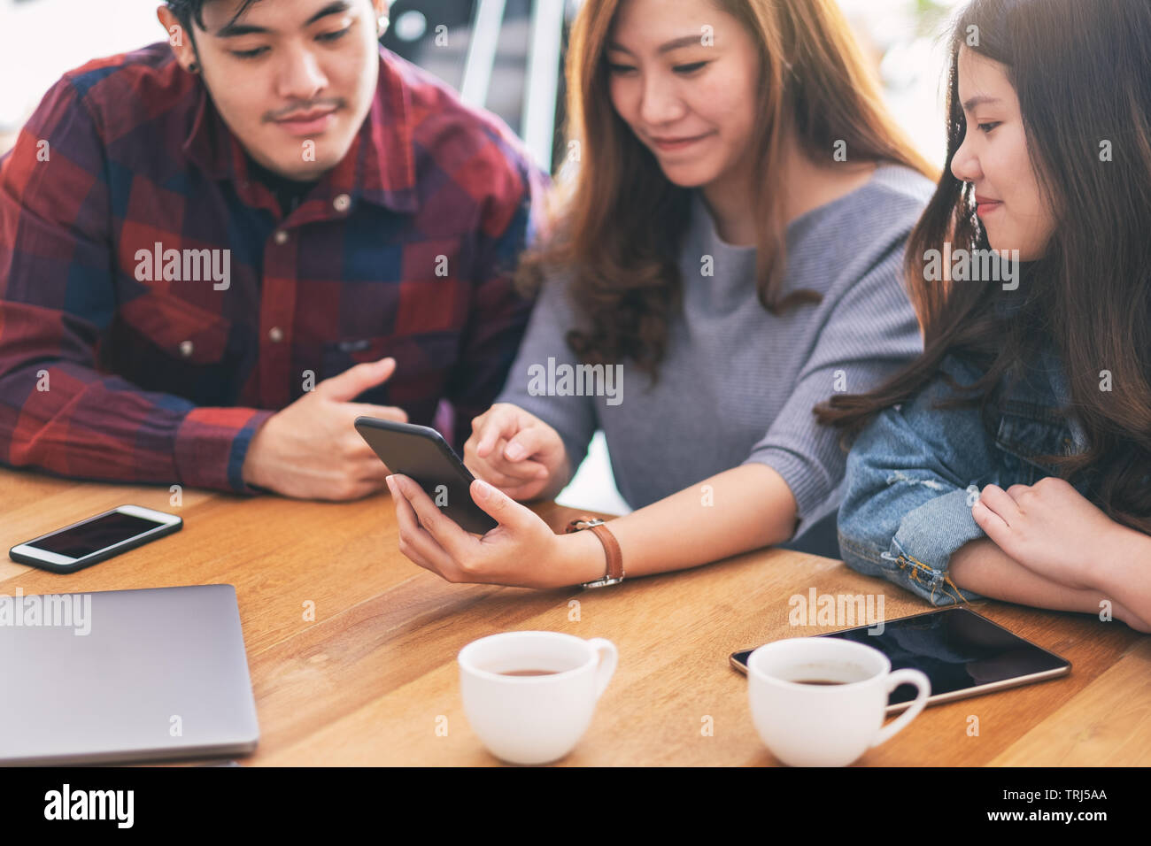 Tres jóvenes asiáticos y mirando a la gente usando el mismo móvil juntos Foto de stock