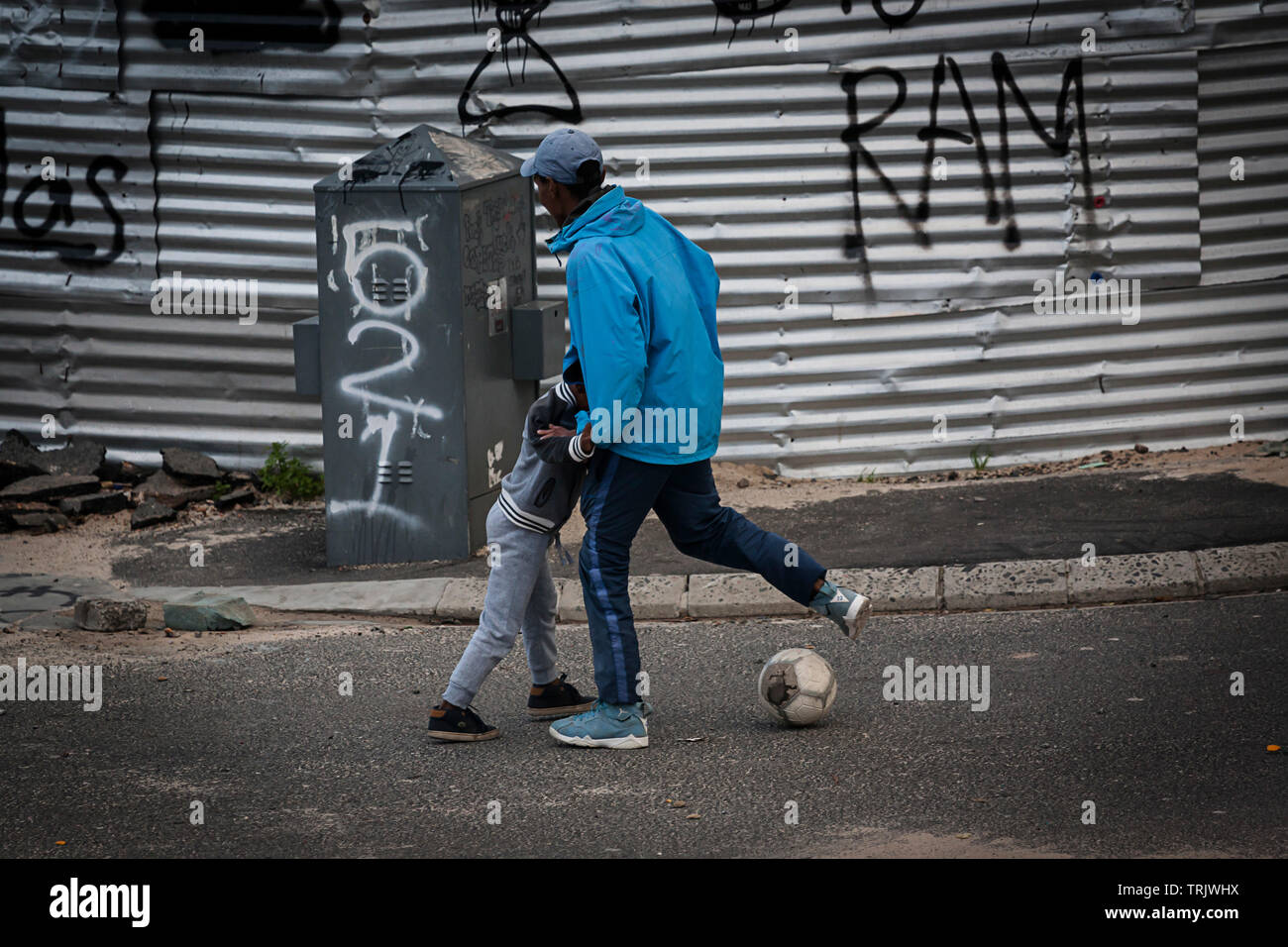 Dos muchachos jugando con una pelota de fútbol en las calles de una barriada en África Foto de stock