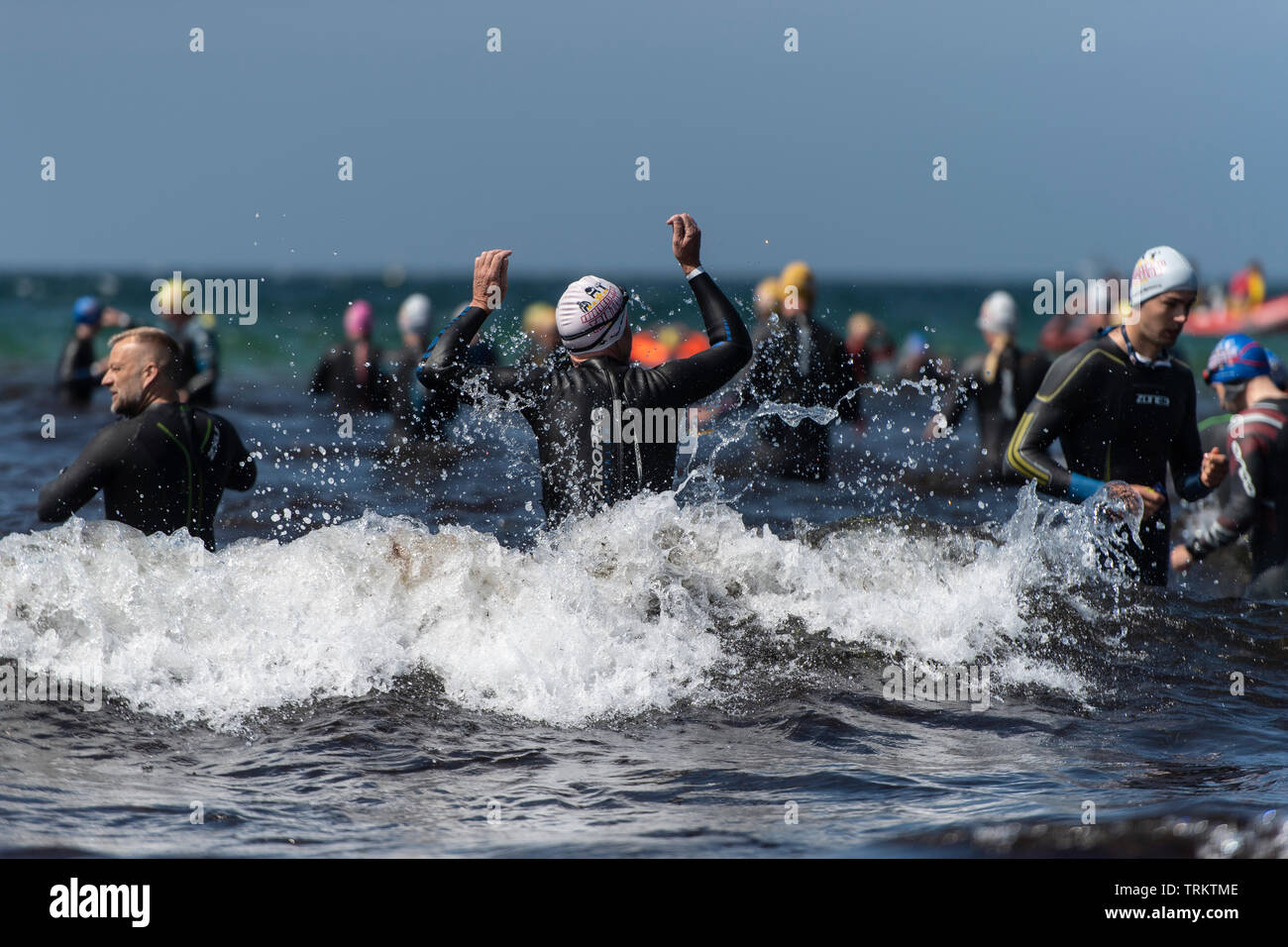 Grandes grupos de triatlón contendientes girando en el mar durante el Triatlón Karrebaeksminde en Dinamarca. Los participantes se visten trajes de neopreno. Foto de stock